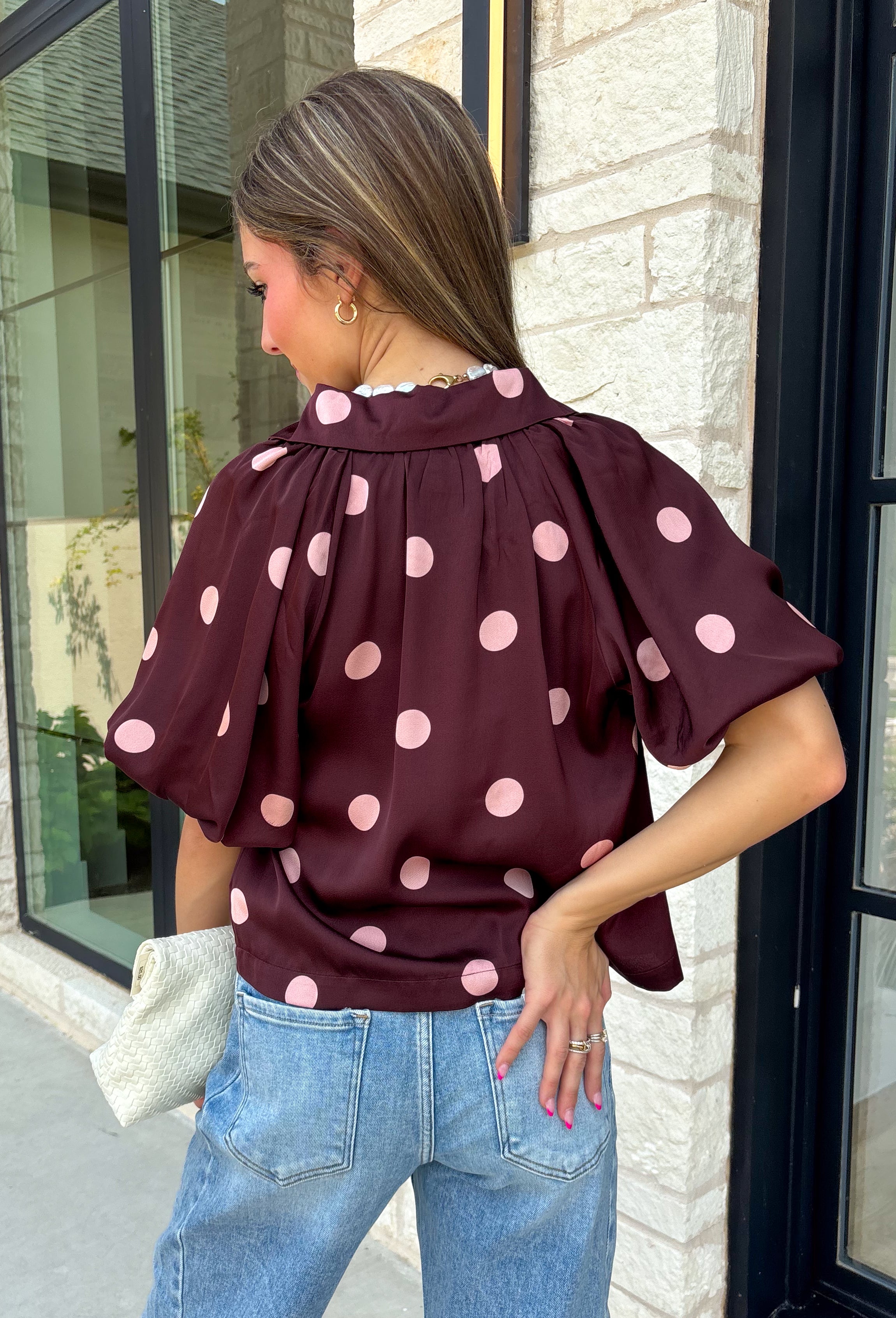 Classic polka dots meet rich fall color in this charming burgundy top! Featuring a soft mauve polka dot print, this top is an effortless way to add personality to your everyday wardrobe. The hidden button front creates a clean, polished look, while the foldover neckline and front pocket add timeless details you'll love. Finished with short puff sleeves, this versatile top is perfect for everything from workdays to weekend brunches and pairs beautifully with your favorite fall denim.