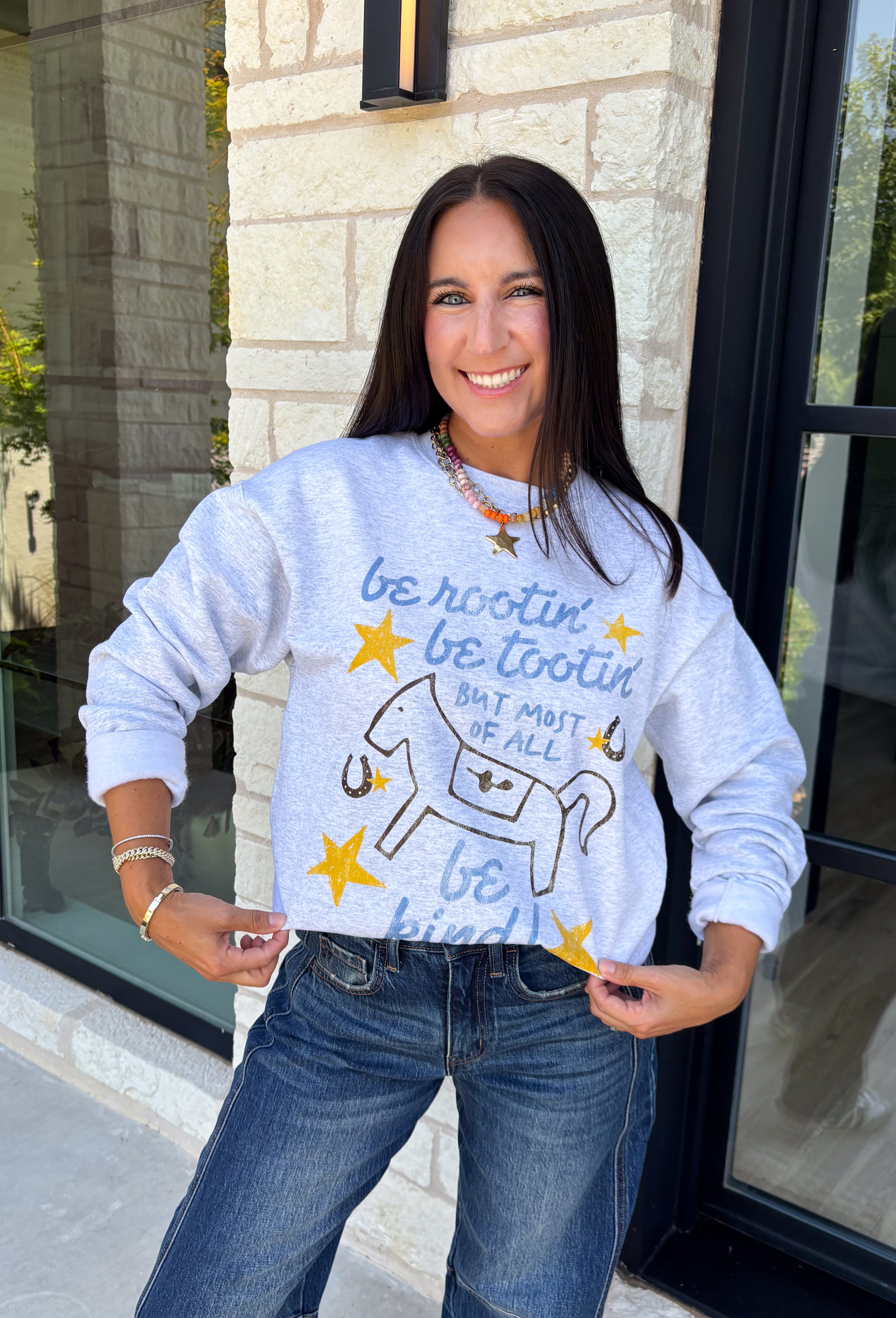 A little western charm and a whole lot of kindness make this sweatshirt an instant favorite! Featuring the playful phrase "Be Rootin', Be Tootin', But Most Of All Be Kind," this heather grey pullover is finished with an abstract illustration of a horse, horseshoe, and stars. The fleece-lined interior keeps you warm and cozy, making it the perfect sweatshirt for everything from weekend errands and football games to bonfires and relaxing at home. 
