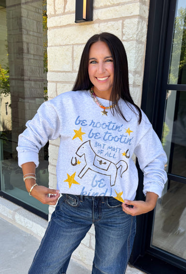 A little western charm and a whole lot of kindness make this sweatshirt an instant favorite! Featuring the playful phrase "Be Rootin', Be Tootin', But Most Of All Be Kind," this heather grey pullover is finished with an abstract illustration of a horse, horseshoe, and stars. The fleece-lined interior keeps you warm and cozy, making it the perfect sweatshirt for everything from weekend errands and football games to bonfires and relaxing at home. 
