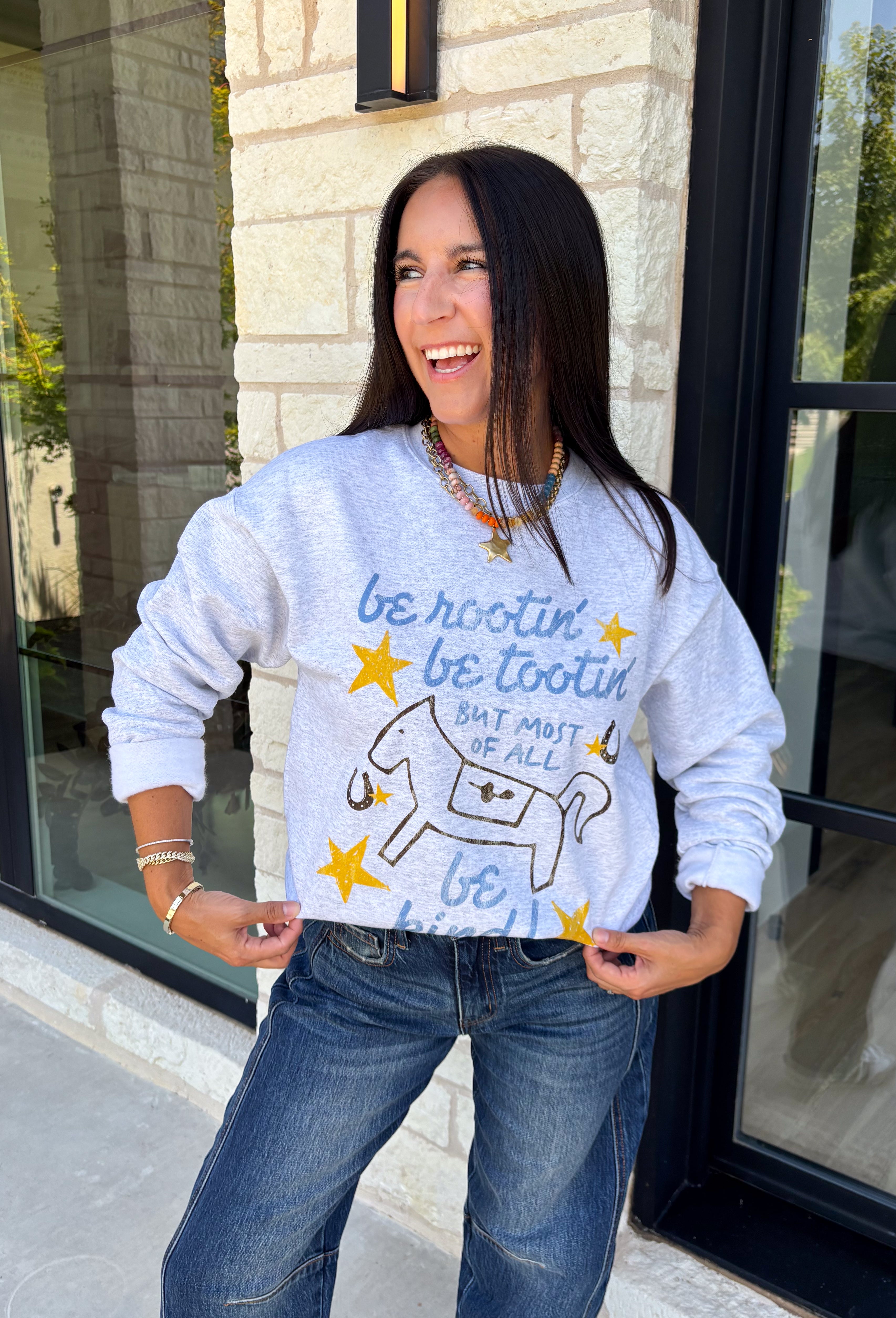 A little western charm and a whole lot of kindness make this sweatshirt an instant favorite! Featuring the playful phrase "Be Rootin', Be Tootin', But Most Of All Be Kind," this heather grey pullover is finished with an abstract illustration of a horse, horseshoe, and stars. The fleece-lined interior keeps you warm and cozy, making it the perfect sweatshirt for everything from weekend errands and football games to bonfires and relaxing at home. 
