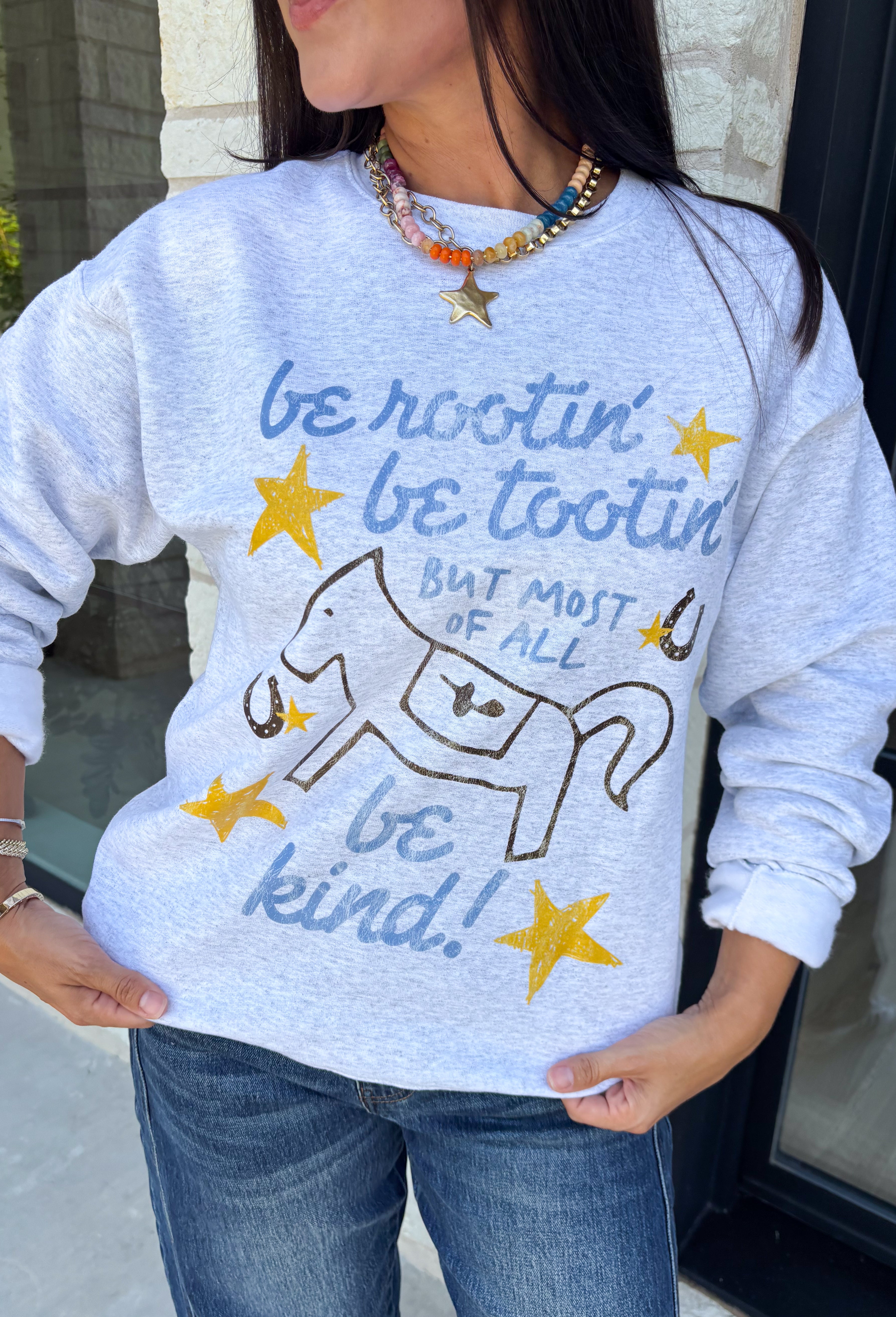 A little western charm and a whole lot of kindness make this sweatshirt an instant favorite! Featuring the playful phrase "Be Rootin', Be Tootin', But Most Of All Be Kind," this heather grey pullover is finished with an abstract illustration of a horse, horseshoe, and stars. The fleece-lined interior keeps you warm and cozy, making it the perfect sweatshirt for everything from weekend errands and football games to bonfires and relaxing at home. 