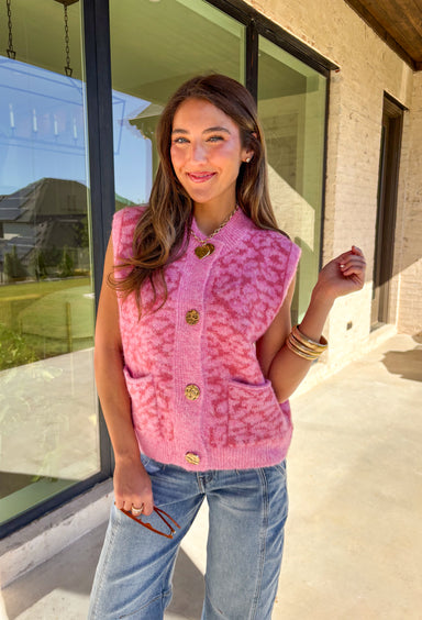 Add a touch of playful charm to your look with this shades-of-pink leopard print sleeveless sweater by &amp;Merci. Crafted in a soft, cozy knit, this piece features shiny gold buttons and two front pockets for a fun, vintage-inspired finish. The sleeveless design makes it perfect for layering or wearing solo during the warmer fall days.