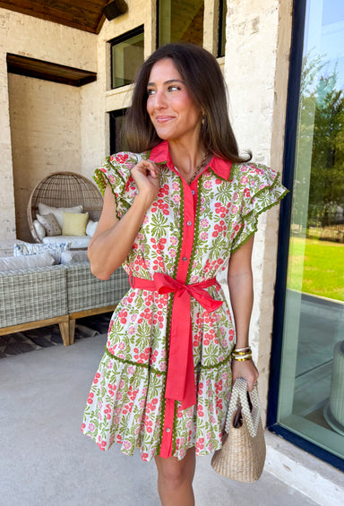 Fresh, feminine, and full of springtime charm, this off white midi dress is blooming with coral, green, and pink florals that instantly brighten your day. The collared neckline and button-down design give it a classic shirt dress feel, while the coral trim and green rick rack detailing along the front, skirt, and sleeves add the sweetest pop of playful contrast. The coral self-tie belt cinches the waist for a flattering silhouette that’s easy to adjust just how you like it.