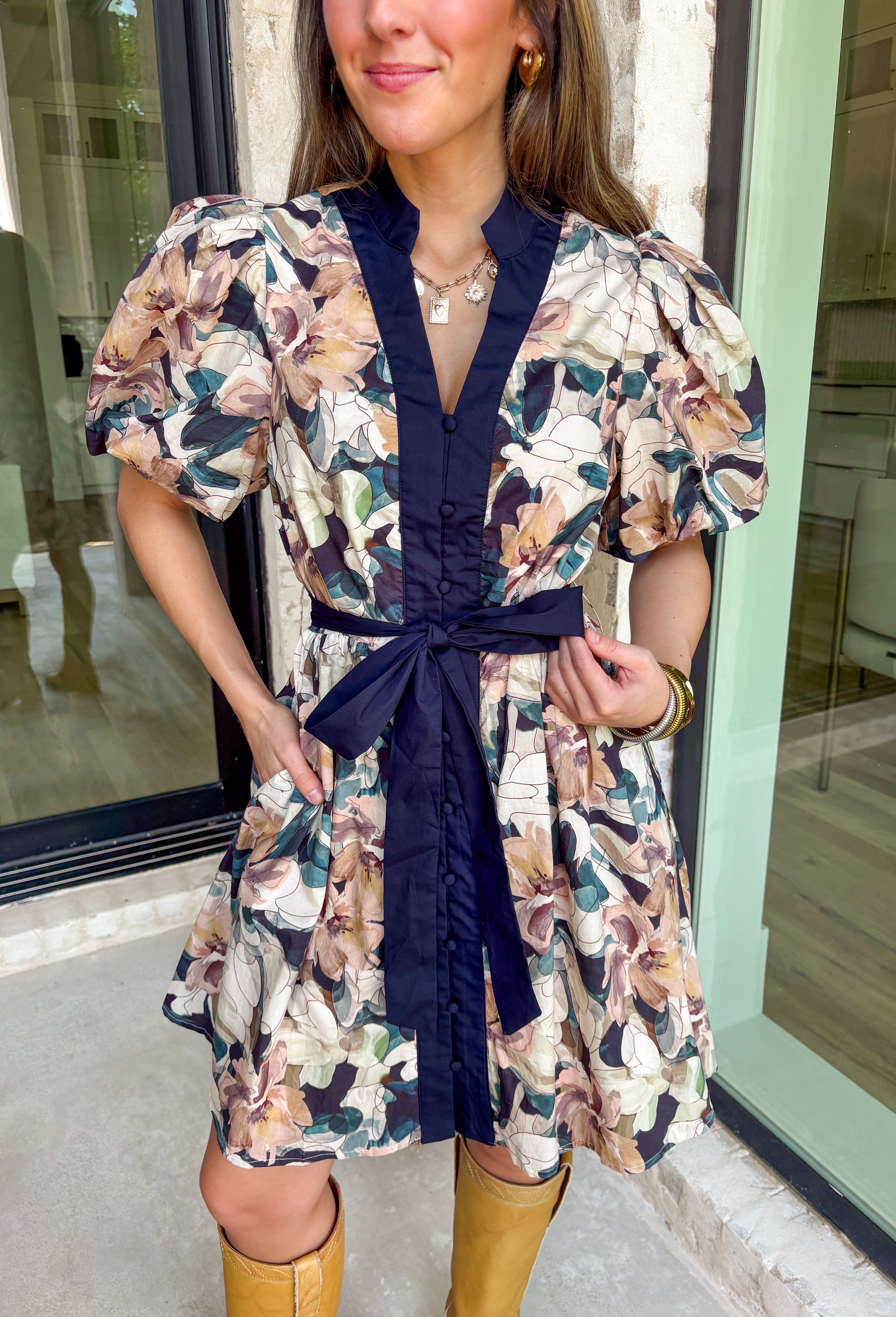 This navy floral dress is giving fall fabulous in the best way. With bold neutral blooms in cream, tan, teal, and brown, it’s the kind of that's perfect for any special occasion. The button-down design and matching self-tie waist keep things polished, while puff sleeves and navy trim down the front add a little extra charm.&nbsp;