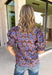 Fresh florals meet rich autumn colors in this beautifully feminine top. Featuring a warm brown backdrop with blooms in shades of blue, purple, and green, this top is an effortless way to brighten your fall wardrobe. The ruffled accent neckline and flattering v-neck add timeless charm, while the short puff sleeves with elastic ruffle cuffs create a soft, romantic silhouette. 