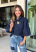 Give your denim collection a fresh twist with this dark wash blouse from Entro. The lightweight cotton fabric keeps it comfortable and easy to wear, while the rich dark wash feels right at home as fall transitions into winter. A high neckline with a self-tie detail adds a pretty focal point, complemented by gold button detailing along the front. The ¾ puff sleeves bring a little volume to the silhouette without making it feel overly dressy. 