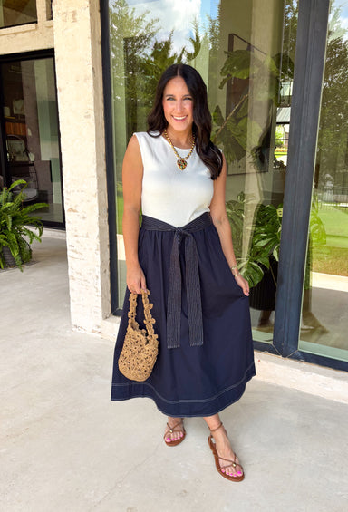 This sleeveless midi dress is the definition of effortless summer style! With its white top and navy skirt design, it gives you that perfectly layered look without any extra effort. The self-tie belt with white threading detail adds a flattering touch at the waist, while the matching detail along the hem pulls everything together beautifully. Lightweight, lined, and finished with side pockets, it’s as practical as it is polished. 