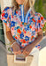 This colorful floral top is pure sunshine in clothing form! With its bright, happy print, it instantly lifts your whole outfit and mood. The blue and white trim along the neckline adds a fun contrast detail, while the puff sleeves give it that soft, feminine shape that’s so easy to wear. Lightweight with a comfortable stretch, it’s perfect for warm days when you want something cheerful and effortless. 