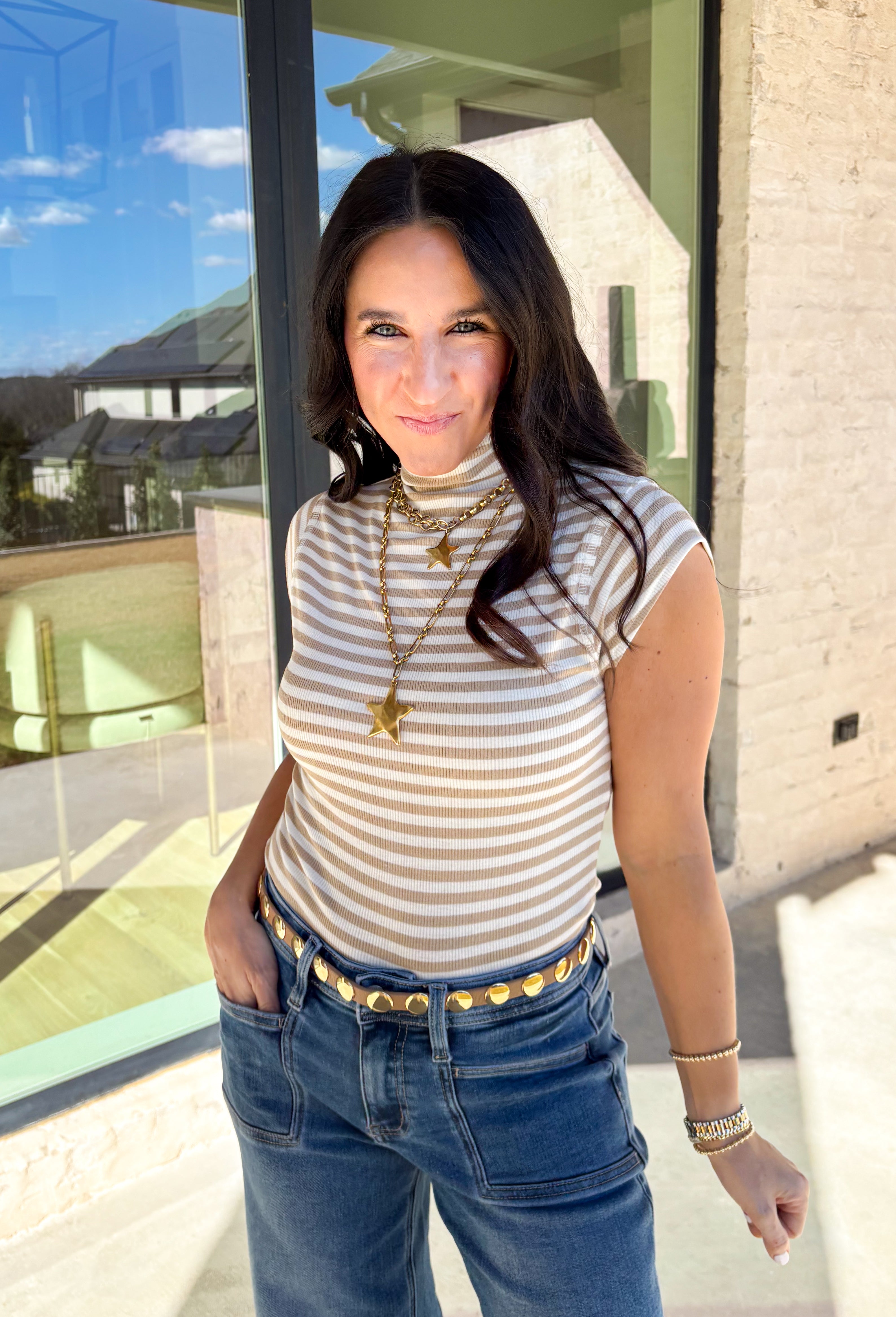 Fresh, fun, and perfect for spring styling, this oatmeal and off-white striped mock neck top by Entro is an easy favorite for the season. Designed with cap sleeves and a lightweight feel, it’s great for warm days while still offering a little extra coverage. The cropped length gives it a modern, on-trend look that pairs perfectly with high-waisted denim, skirts, or trousers.