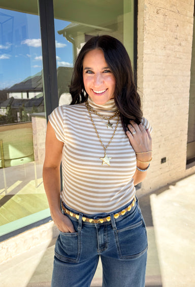 Fresh, fun, and perfect for spring styling, this oatmeal and off-white striped mock neck top by Entro is an easy favorite for the season. Designed with cap sleeves and a lightweight feel, it’s great for warm days while still offering a little extra coverage. The cropped length gives it a modern, on-trend look that pairs perfectly with high-waisted denim, skirts, or trousers.