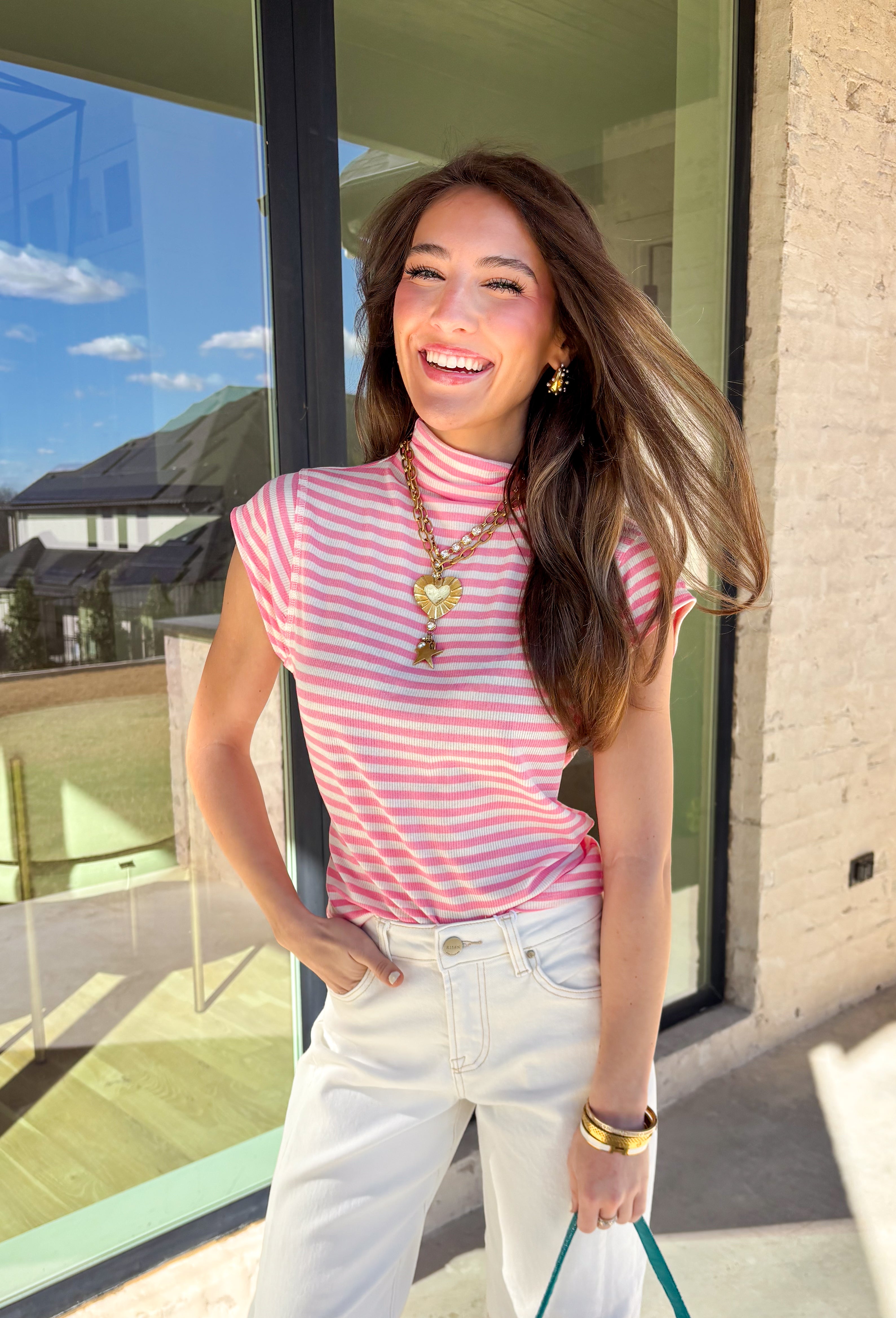 Fresh, fun, and perfect for spring styling, this pink and off-white striped mock neck top by Entro is an easy favorite for the season. Designed with cap sleeves and a lightweight feel, it’s great for warm days while still offering a little extra coverage. The cropped length gives it a modern, on-trend look that pairs perfectly with high-waisted denim, skirts, or trousers.