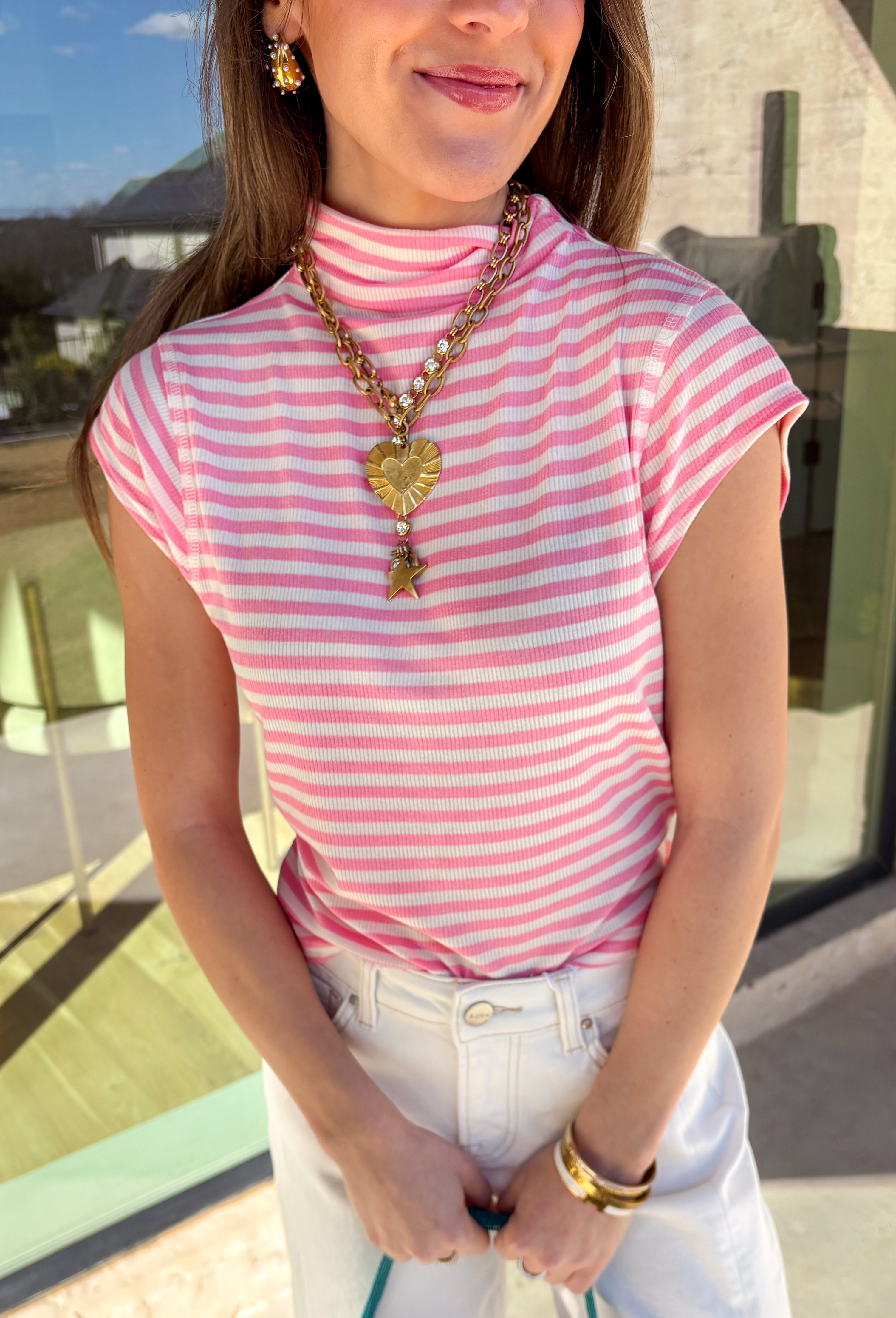 Fresh, fun, and perfect for spring styling, this pink and off-white striped mock neck top by Entro is an easy favorite for the season. Designed with cap sleeves and a lightweight feel, it’s great for warm days while still offering a little extra coverage. The cropped length gives it a modern, on-trend look that pairs perfectly with high-waisted denim, skirts, or trousers.