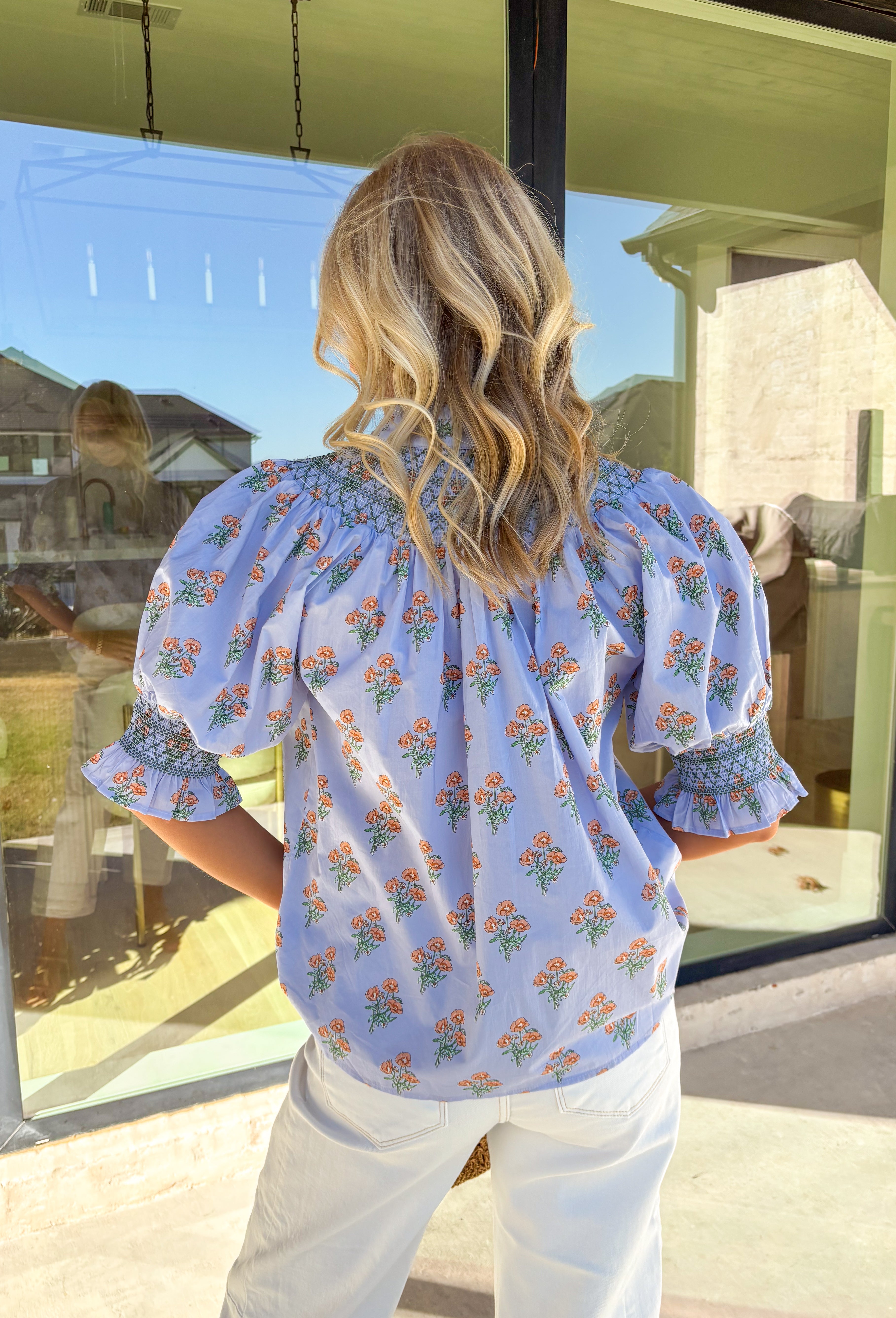 Light, airy, and full of spring charm, this light blue button-down top by Entro is an easy favorite for the season. Featuring a soft peach and green floral print, it feels fresh and cheerful without being overpowering. Smocking along the sleeves, neckline, and back adds texture and a comfortable, flattering fit, while the subtle ruffle neckline and sleeve details give it a sweet, feminine finish. Crafted from breathable cotton, this top is perfect for sunny days and easy layering.
