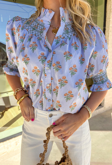 Light, airy, and full of spring charm, this light blue button-down top by Entro is an easy favorite for the season. Featuring a soft peach and green floral print, it feels fresh and cheerful without being overpowering. Smocking along the sleeves, neckline, and back adds texture and a comfortable, flattering fit, while the subtle ruffle neckline and sleeve details give it a sweet, feminine finish. Crafted from breathable cotton, this top is perfect for sunny days and easy layering.