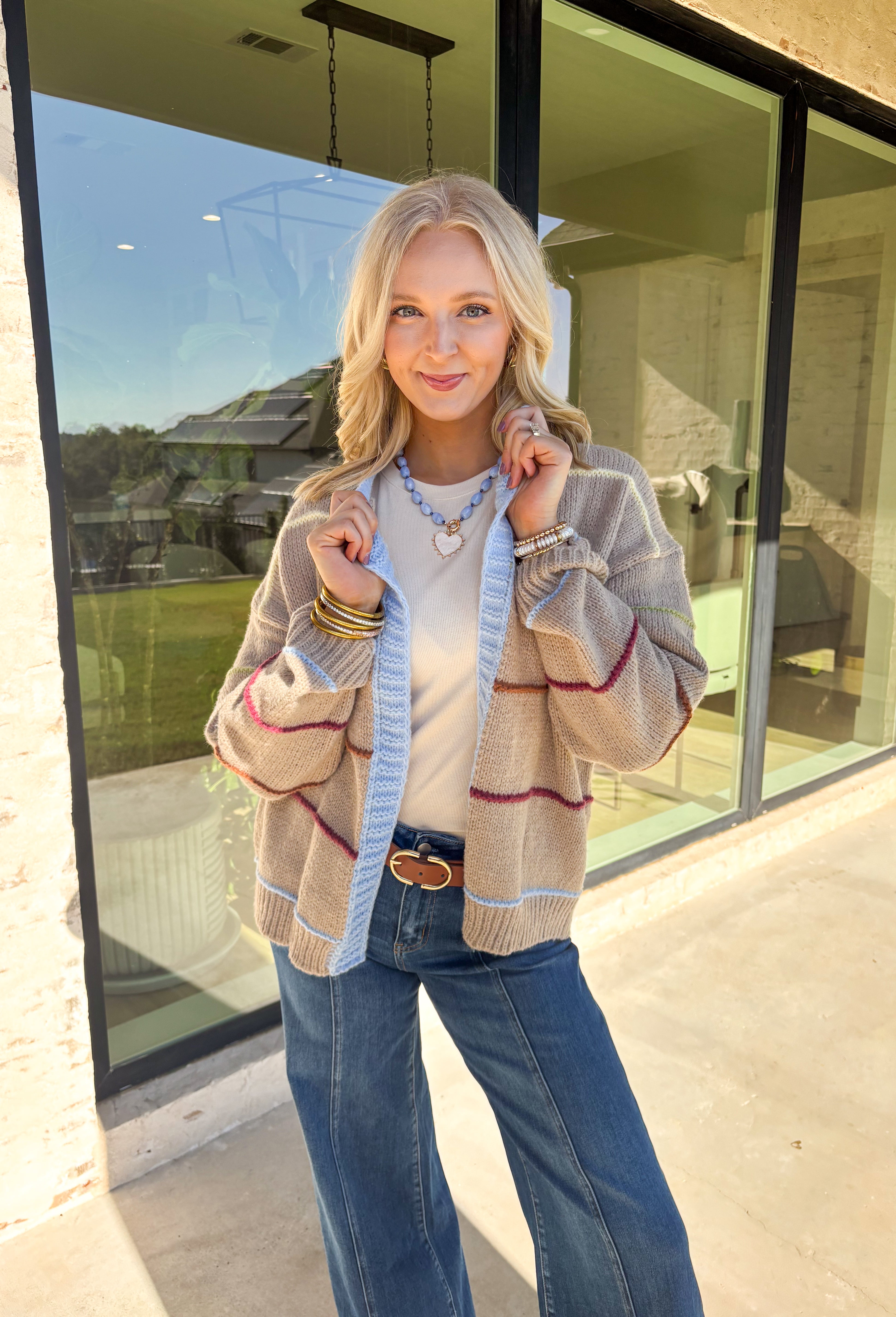 Cozy, colorful, and perfect for layering—this tan knit cardigan is a must-have for your fall wardrobe. Designed with bold stripes in burgundy, brown, green, light yellow, and light blue, it’s finished with light blue trim along the neckline and edges for a playful pop. The soft knit makes it warm without being heavy, giving you the ideal piece to throw over basics or style with denim and dresses alike.
