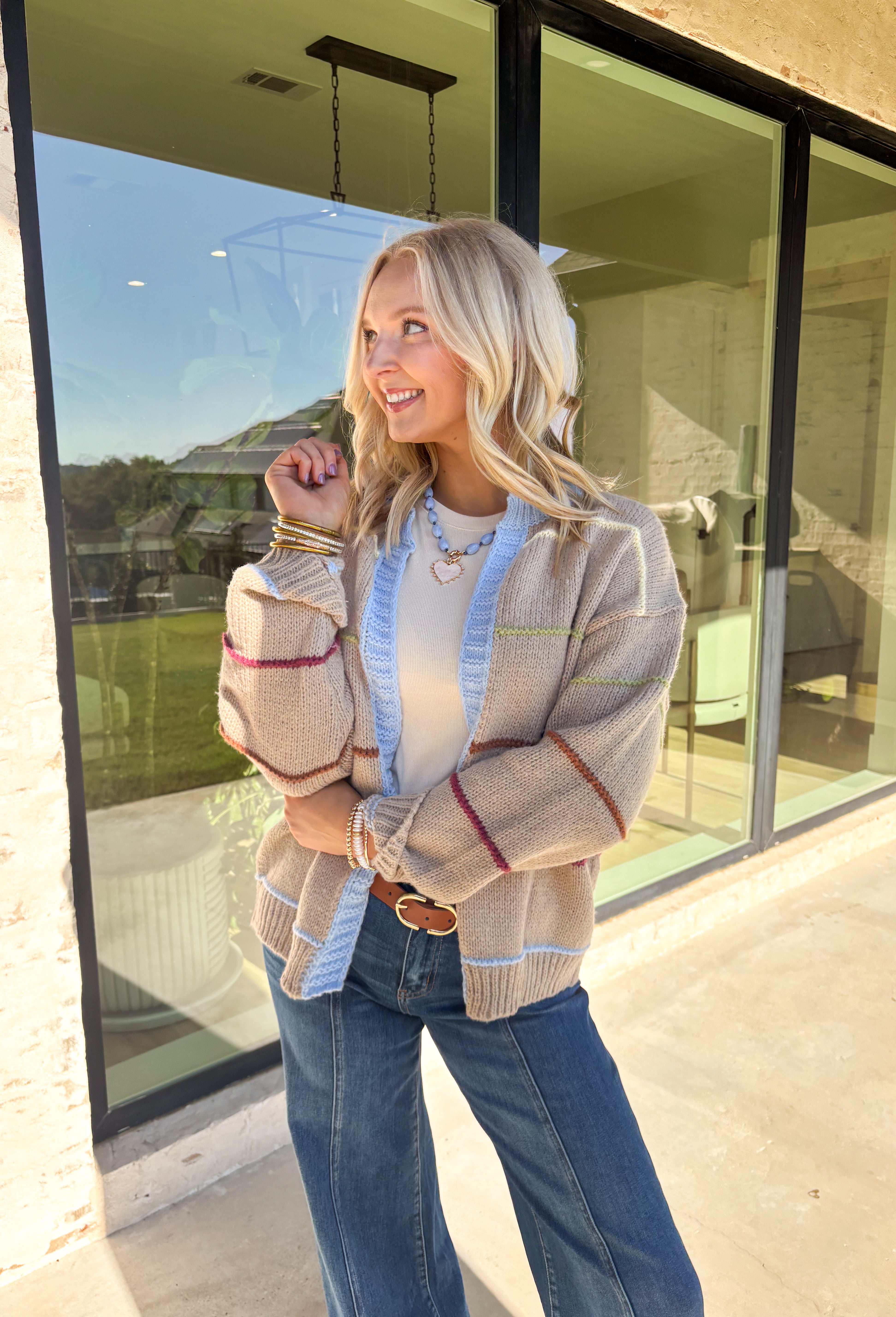 Cozy, colorful, and perfect for layering—this tan knit cardigan is a must-have for your fall wardrobe. Designed with bold stripes in burgundy, brown, green, light yellow, and light blue, it’s finished with light blue trim along the neckline and edges for a playful pop. The soft knit makes it warm without being heavy, giving you the ideal piece to throw over basics or style with denim and dresses alike.