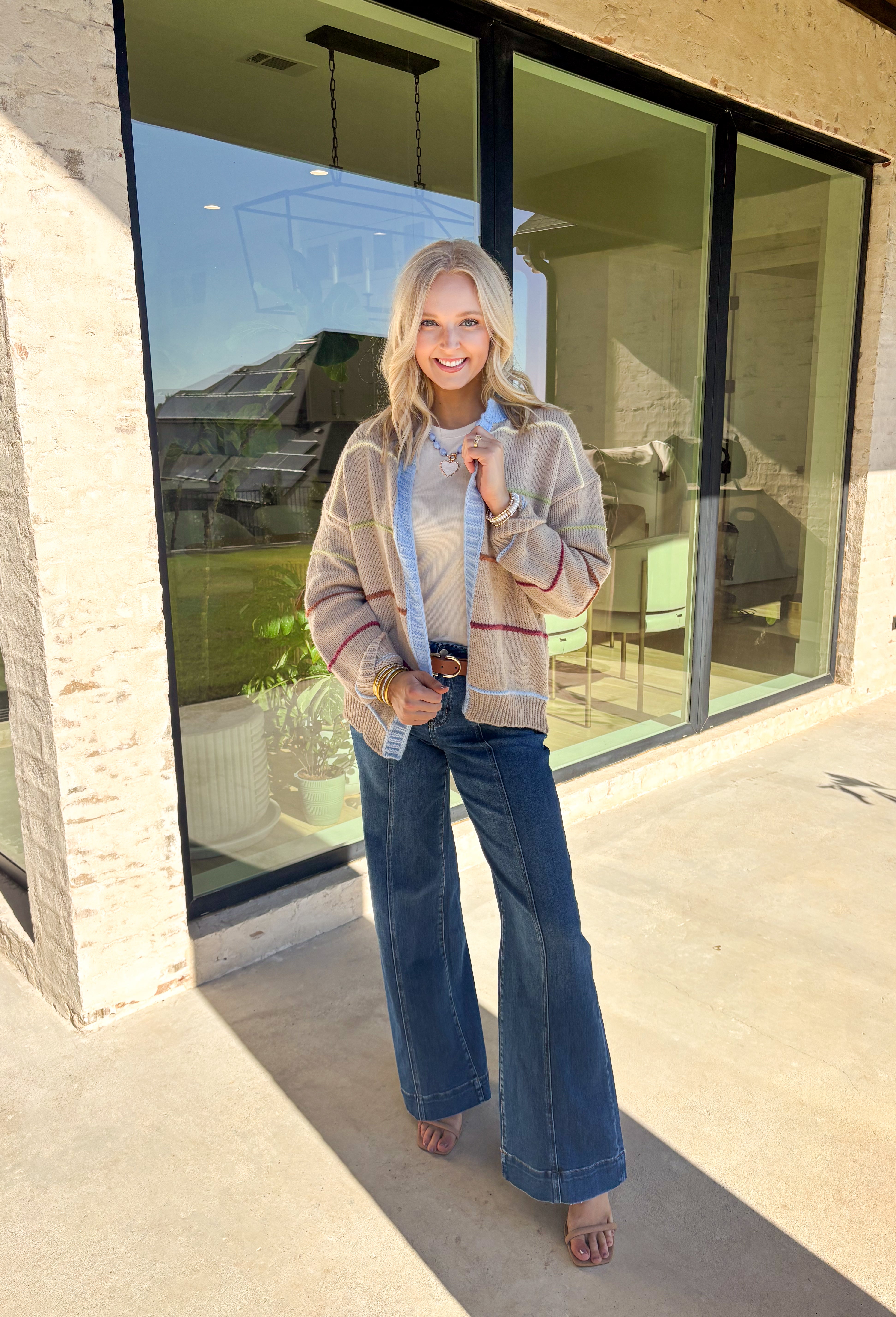Cozy, colorful, and perfect for layering—this tan knit cardigan is a must-have for your fall wardrobe. Designed with bold stripes in burgundy, brown, green, light yellow, and light blue, it’s finished with light blue trim along the neckline and edges for a playful pop. The soft knit makes it warm without being heavy, giving you the ideal piece to throw over basics or style with denim and dresses alike.