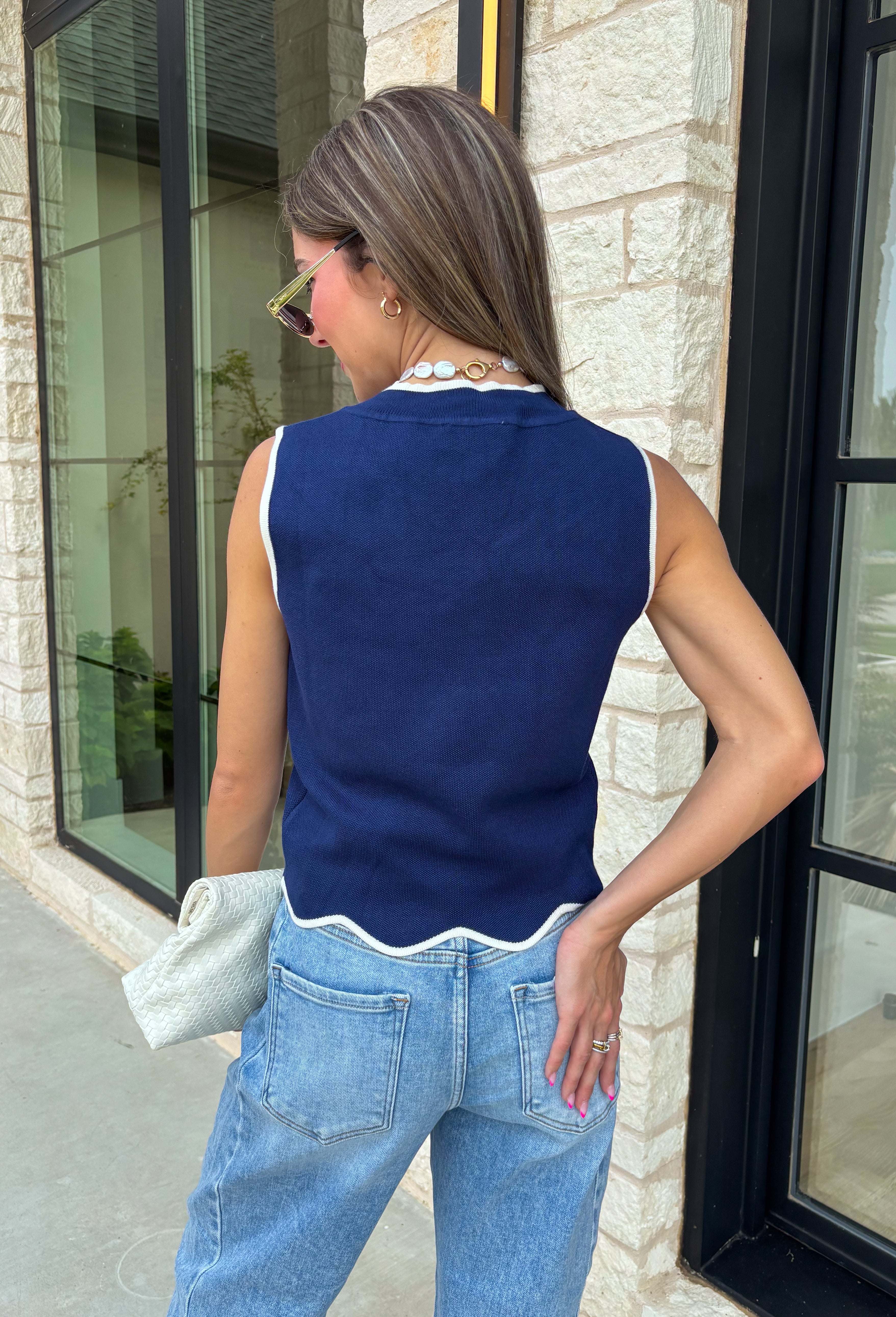Classic with a touch of charm, this navy sweater tank is made for the season ahead. The rich autumn hue is beautifully accented with crisp white trim and a delicate scalloped hem, creating a timeless look that's both polished and playful. Crafted from a soft sweater knit, it's perfect for layering under your favorite blazer, denim jacket, or cardigan as the temperatures begin to cool. 