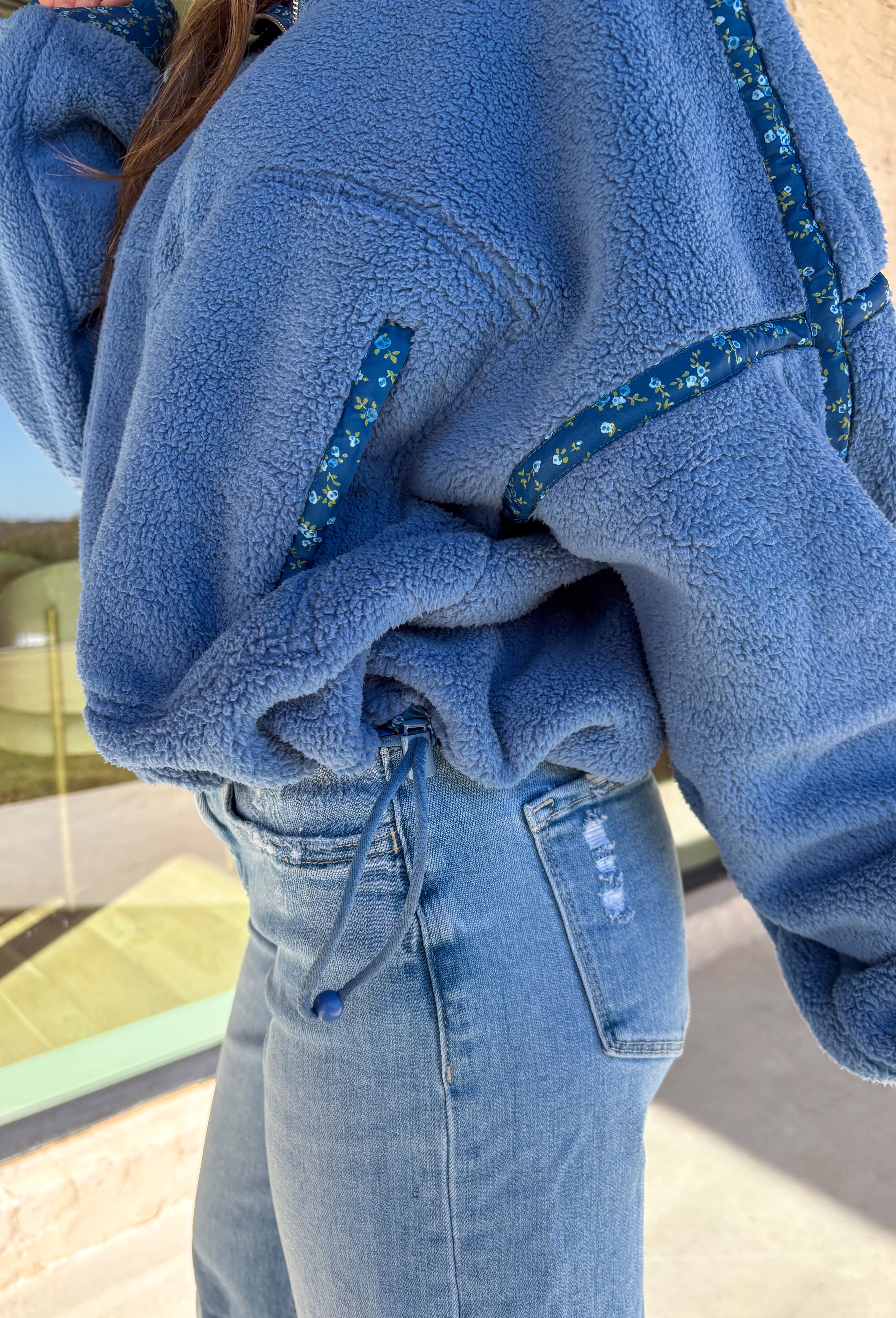 Bundle up in cozy comfort with this blue sherpa pullover by Peach Love. Featuring soft fleece fabric and a subtle floral print along the trim, this quarter-zip adds the perfect touch of femininity to a winter classic. The navy floral accents give it just the right amount of color, while the front pockets and plush texture make it a cold-weather favorite for lounging or layering.