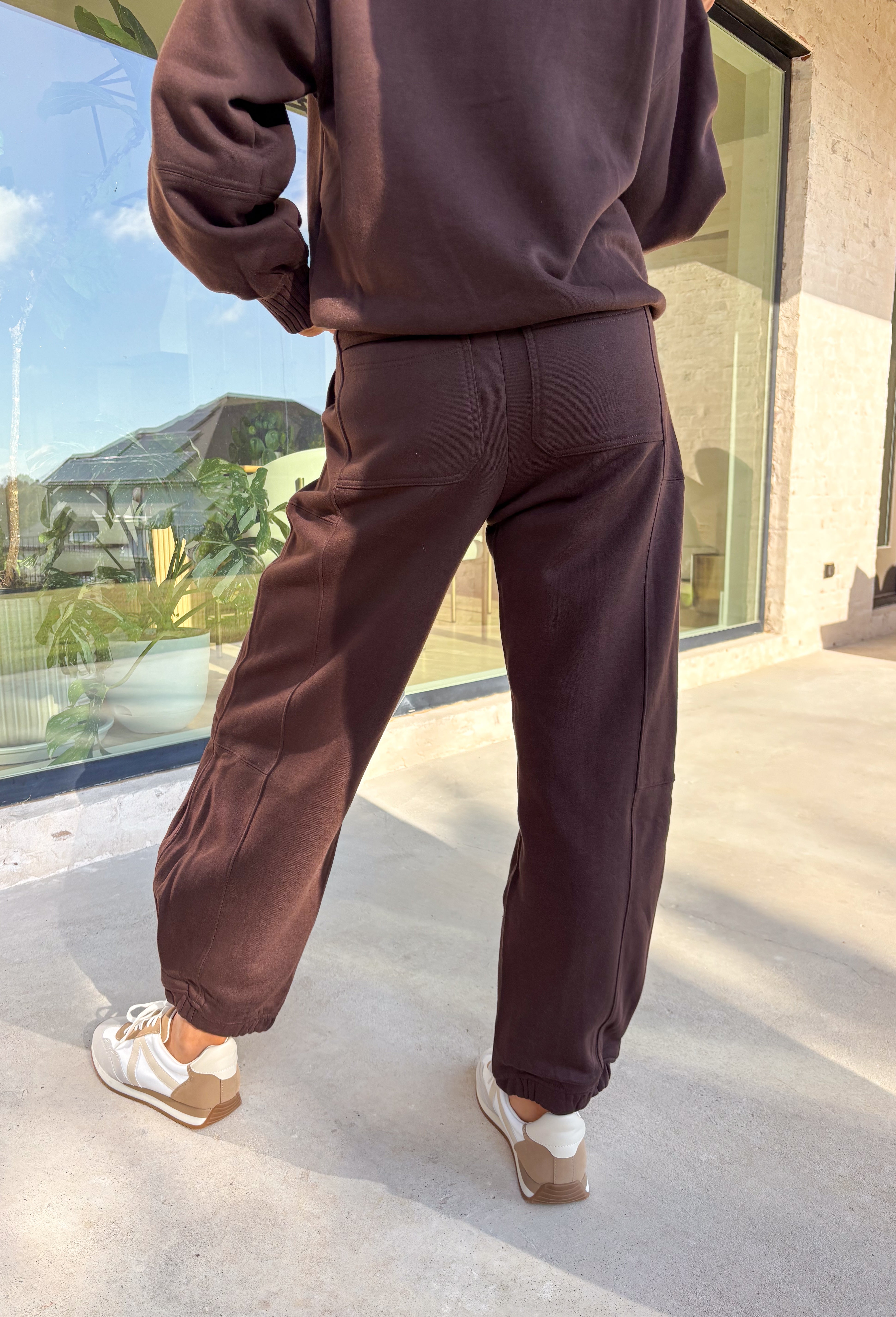 Stay cozy in style with these chocolate brown barrel joggers by Rae Mode. Lined in soft fleece and finished with a drawstring elastic waistband, these joggers offer the perfect blend of comfort and warmth for chilly winter days. Featuring side and back pockets for everyday convenience, their relaxed barrel silhouette makes them ideal for lounging or layering on the go. Pair them with the matching quarter-zip pullover for a complete cozy set or wear them solo for a laid-back, stylish look.