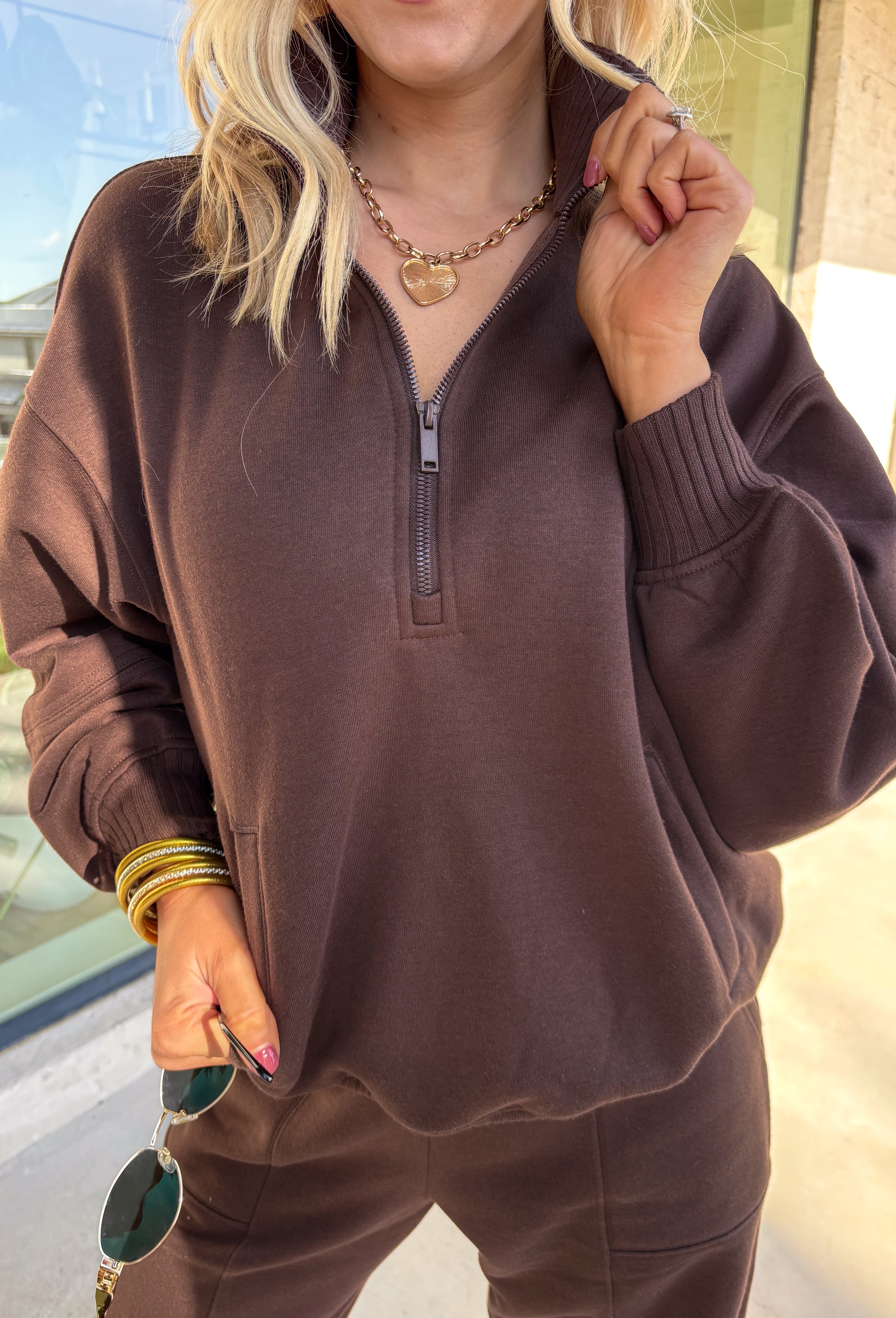 Cozy up this winter in the chocolate brown fleece quarter zip pullover by Rae Mode. Designed with ribbed detailing along the collar, hem, and sleeve cuffs, this pullover combines a relaxed fit with an effortlessly polished look. The soft fleece interior and front pockets add extra warmth and comfort, making it the perfect throw-on for chilly days. Pair it with the matching joggers for the full set, or style it solo for an easy, laid-back outfit.