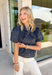 Classic fall patterns and delicate embroidery come together beautifully in this charming top. Featuring a navy and blue checkered print accented with light pink floral embroidery, this top brings a fresh, feminine touch to your autumn wardrobe. The self-tie neckline adds timeless charm, while the short puff sleeves with elastic cuffs create a flattering silhouette that's easy to wear from day to night. 
