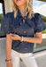 Classic fall patterns and delicate embroidery come together beautifully in this charming top. Featuring a navy and blue checkered print accented with light pink floral embroidery, this top brings a fresh, feminine touch to your autumn wardrobe. The self-tie neckline adds timeless charm, while the short puff sleeves with elastic cuffs create a flattering silhouette that's easy to wear from day to night. 