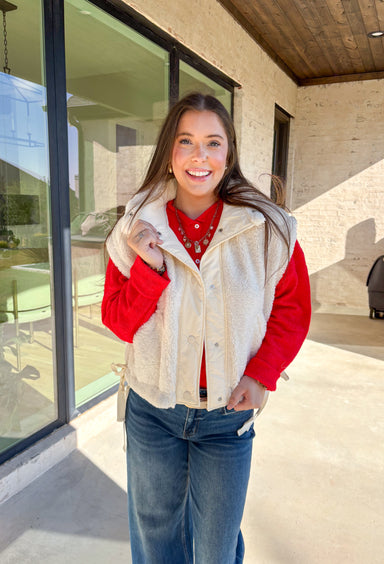Layer on the warmth with this off white sherpa vest, the perfect cozy piece for winter. Designed with a button-down front and ivory trim, it’s accented with side pockets for practicality and tie details on the sides for an adjustable fit. The plush sherpa texture makes it a must-have layering piece, whether you’re throwing it over a chunky sweater or styling it with a casual flannel. This vest blends comfort and style for the season’s coldest days.