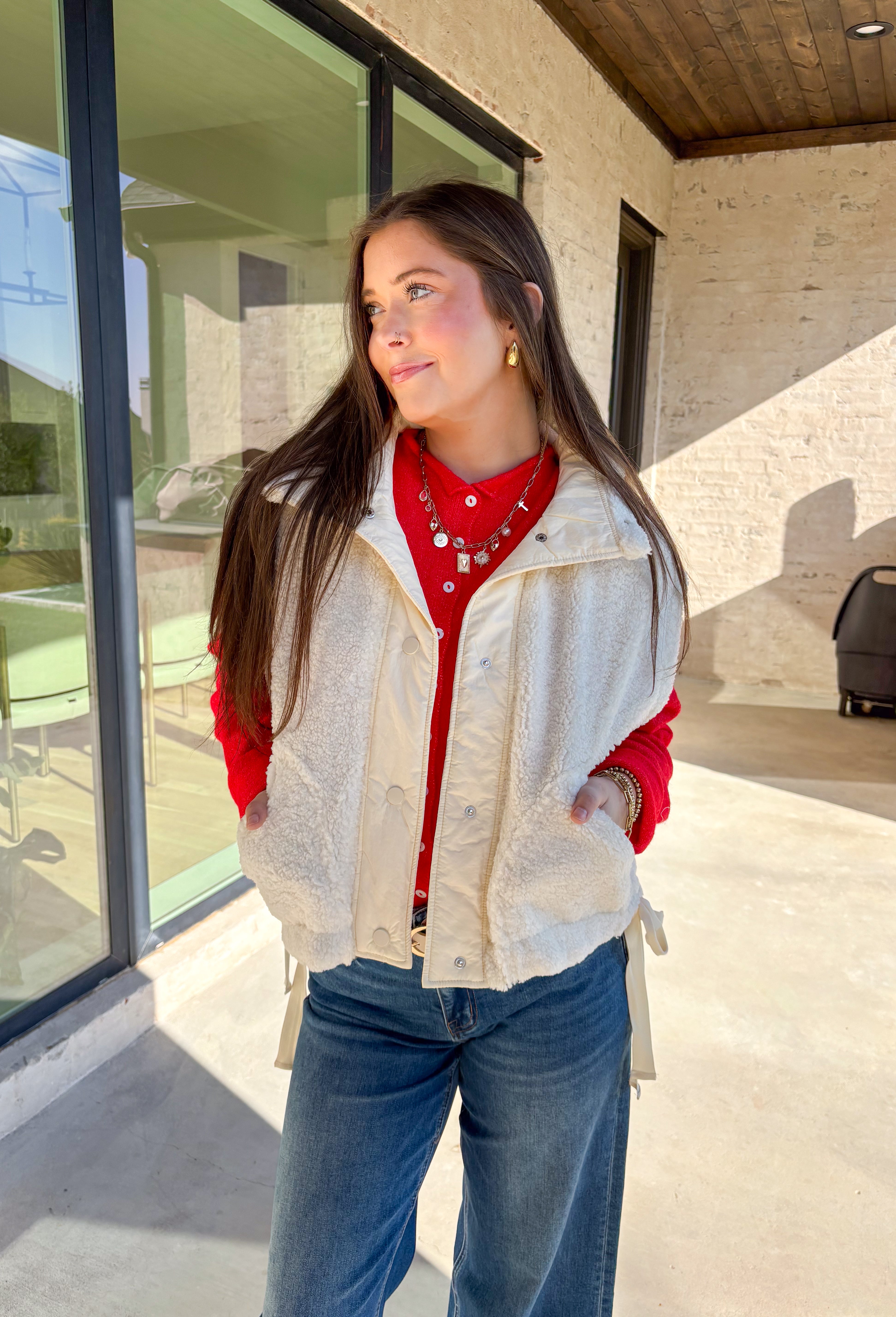 Layer on the warmth with this off white sherpa vest, the perfect cozy piece for winter. Designed with a button-down front and ivory trim, it’s accented with side pockets for practicality and tie details on the sides for an adjustable fit. The plush sherpa texture makes it a must-have layering piece, whether you’re throwing it over a chunky sweater or styling it with a casual flannel. This vest blends comfort and style for the season’s coldest days.