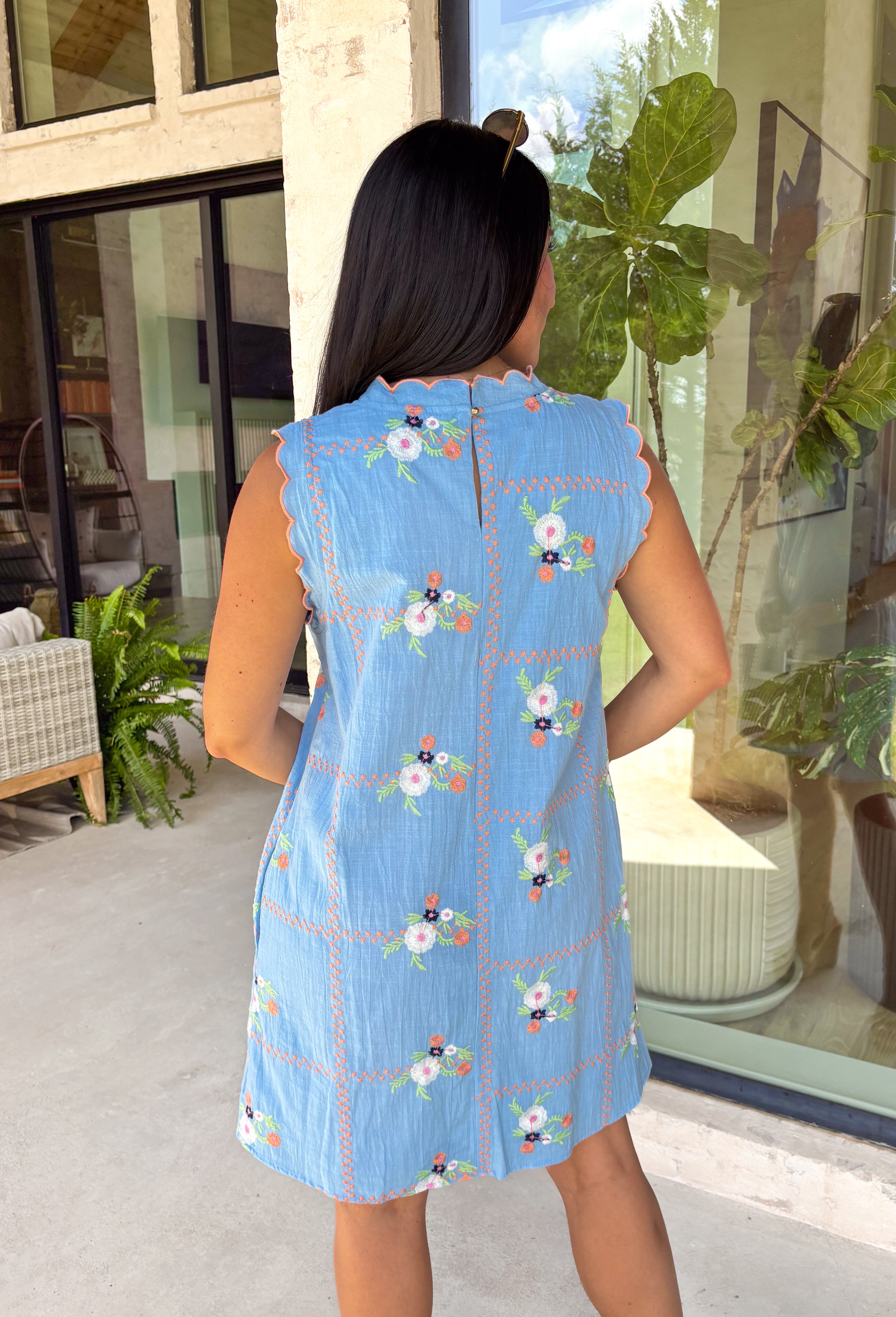 Sweet, sunny, and perfect for spring, this chambray sleeveless dress by Entro is full of charming detail. Designed with colorful floral embroidery in coral, white, navy, and green, it adds a beautiful pop against the soft chambray base. Scalloped trim along the neckline and sleeves gives it a delicate, feminine finish, while the button closure at the back adds a subtle touch of interest. Fully lined and complete with side pockets.