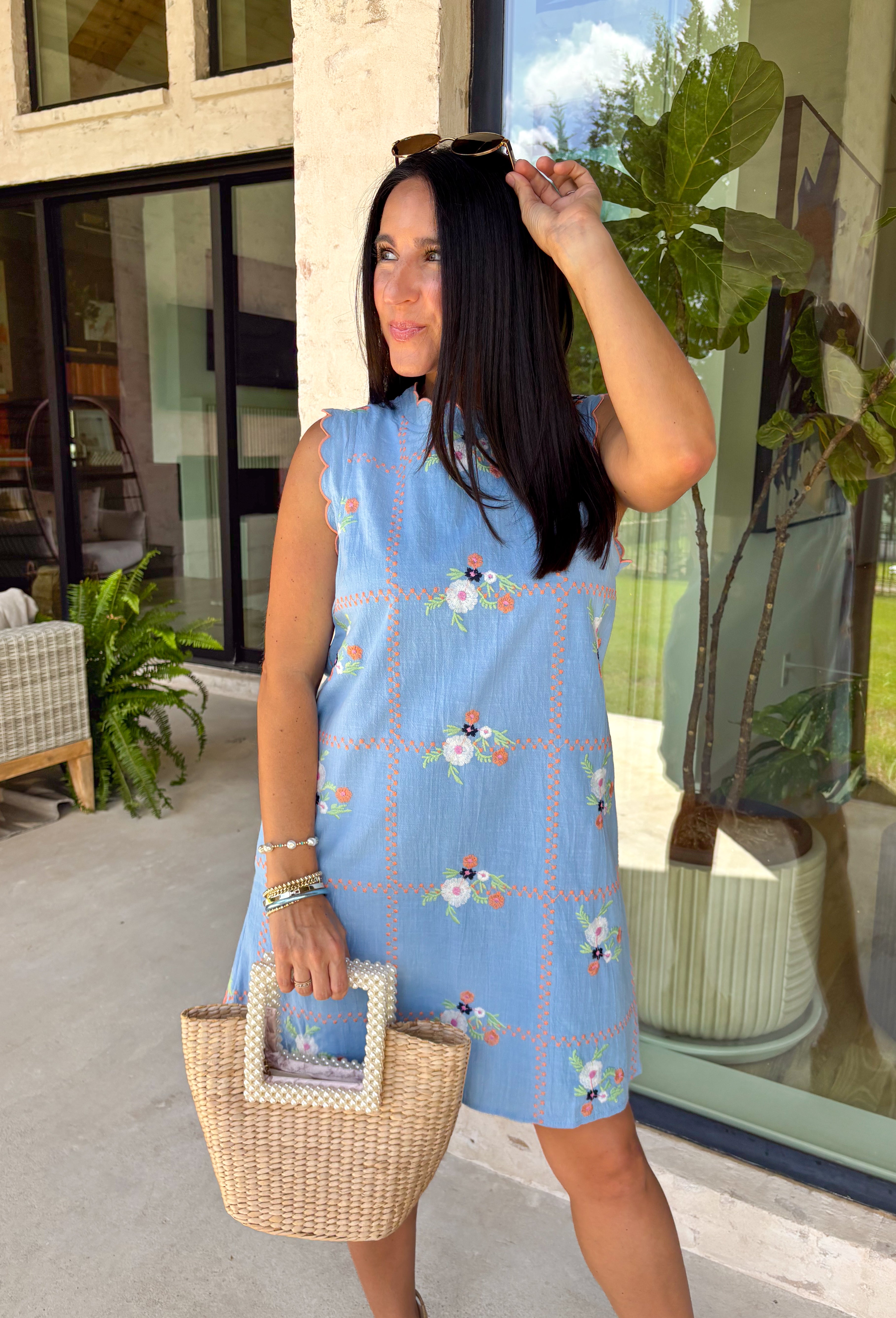 Sweet, sunny, and perfect for spring, this chambray sleeveless dress by Entro is full of charming detail. Designed with colorful floral embroidery in coral, white, navy, and green, it adds a beautiful pop against the soft chambray base. Scalloped trim along the neckline and sleeves gives it a delicate, feminine finish, while the button closure at the back adds a subtle touch of interest. Fully lined and complete with side pockets.
