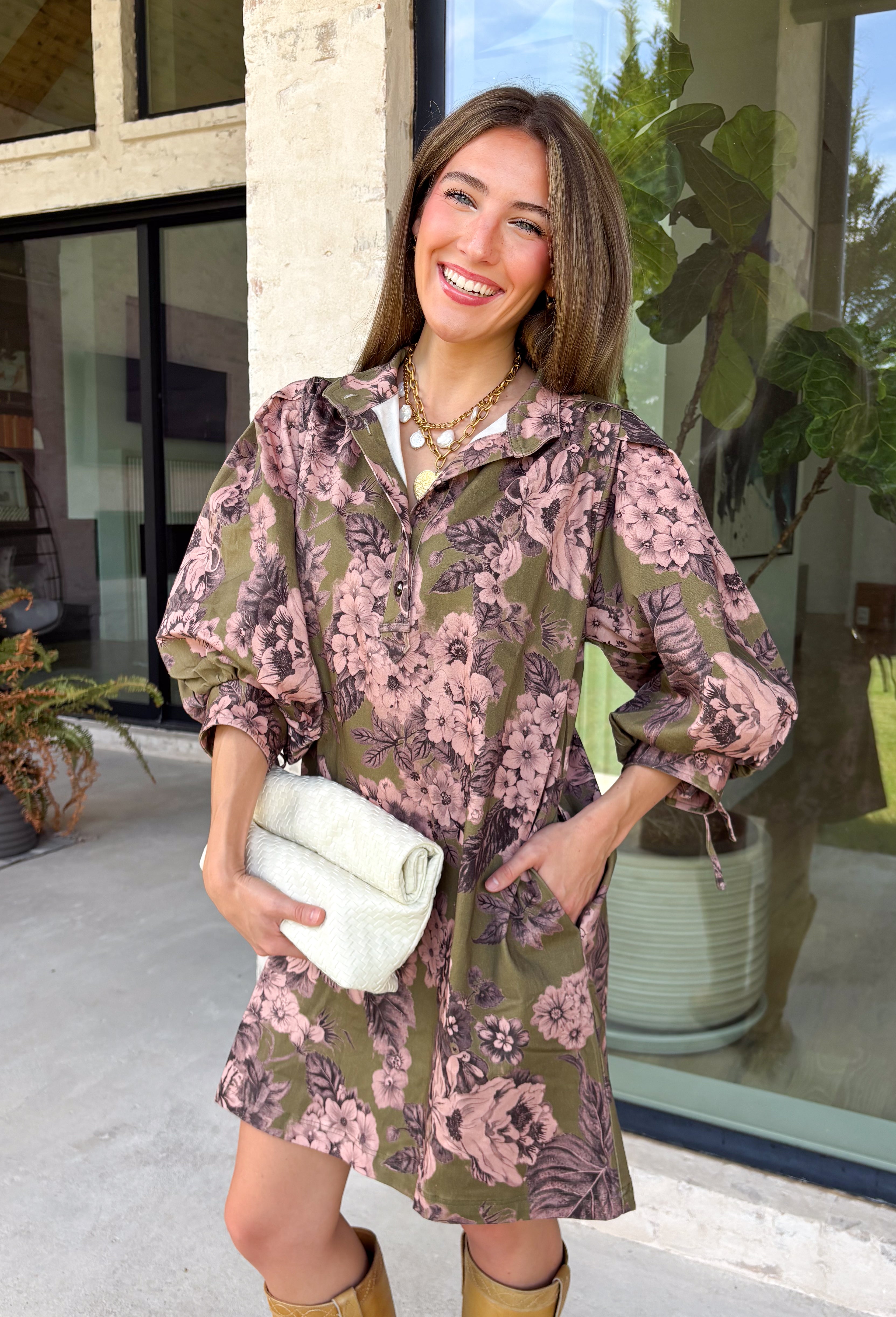 Bring effortless charm to your fall wardrobe with this beautifully detailed dress from Entro. Designed in a rich olive hue with a delicate floral print in shades of light pink and black, this timeless dress is perfect for everything from brunch dates to weekend outings. The stand neckline and partial button-front closure create a polished silhouette, while the ¾ puff sleeves are finished with sweet tie cuffs for an extra feminine touch. 