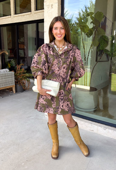 Bring effortless charm to your fall wardrobe with this beautifully detailed dress from Entro. Designed in a rich olive hue with a delicate floral print in shades of light pink and black, this timeless dress is perfect for everything from brunch dates to weekend outings. The stand neckline and partial button-front closure create a polished silhouette, while the ¾ puff sleeves are finished with sweet tie cuffs for an extra feminine touch. 
