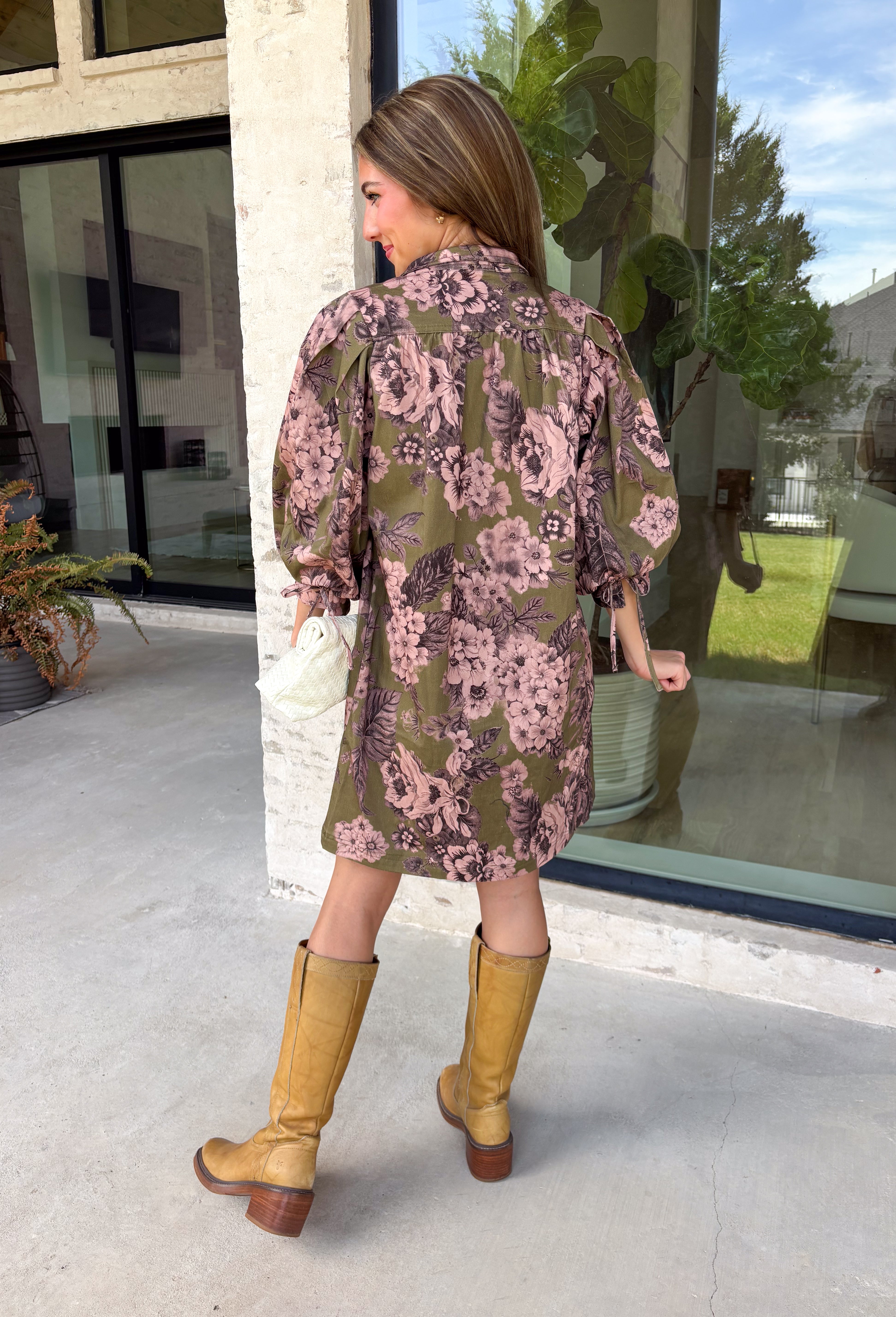 Bring effortless charm to your fall wardrobe with this beautifully detailed dress from Entro. Designed in a rich olive hue with a delicate floral print in shades of light pink and black, this timeless dress is perfect for everything from brunch dates to weekend outings. The stand neckline and partial button-front closure create a polished silhouette, while the ¾ puff sleeves are finished with sweet tie cuffs for an extra feminine touch. 