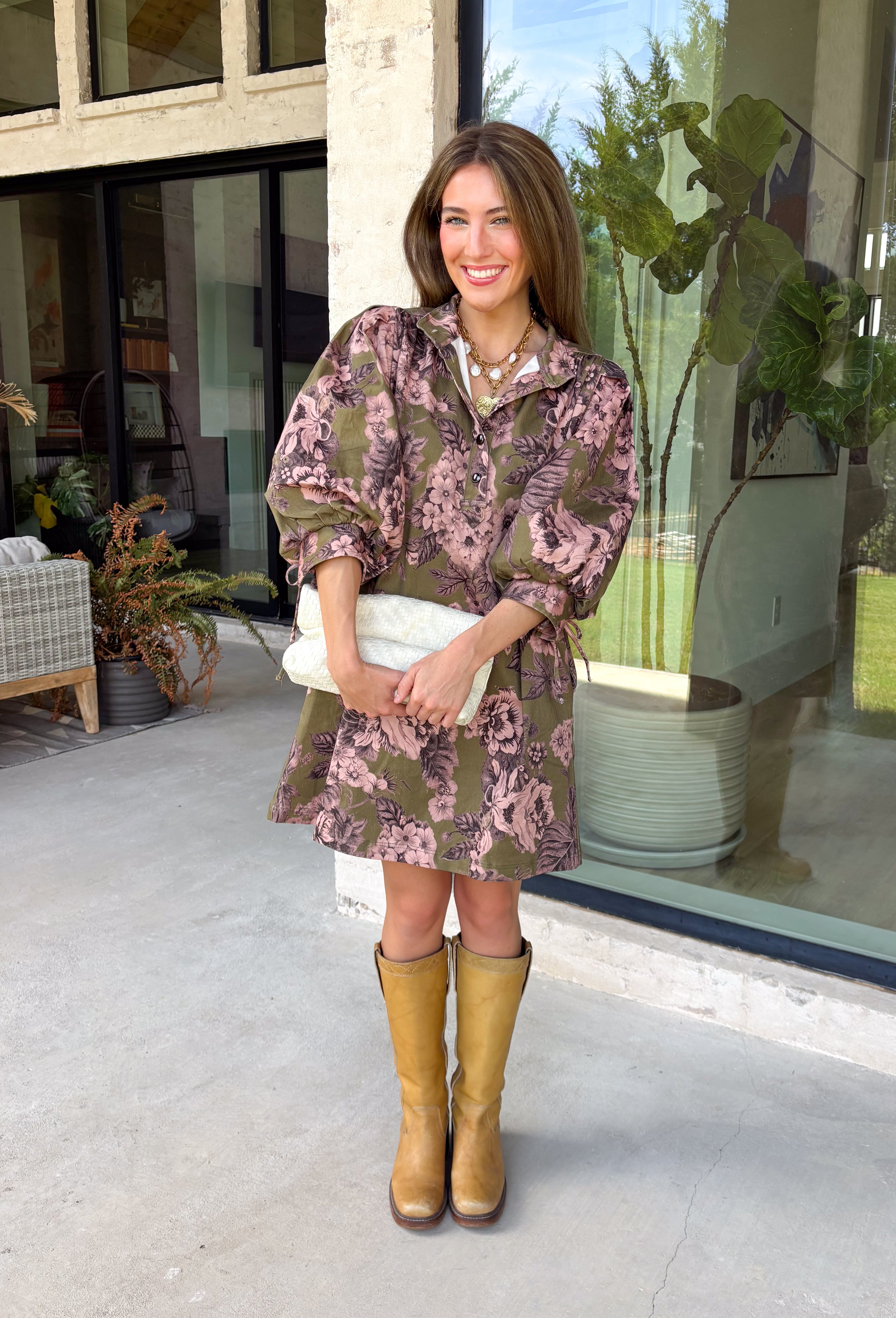 Bring effortless charm to your fall wardrobe with this beautifully detailed dress from Entro. Designed in a rich olive hue with a delicate floral print in shades of light pink and black, this timeless dress is perfect for everything from brunch dates to weekend outings. The stand neckline and partial button-front closure create a polished silhouette, while the ¾ puff sleeves are finished with sweet tie cuffs for an extra feminine touch. 