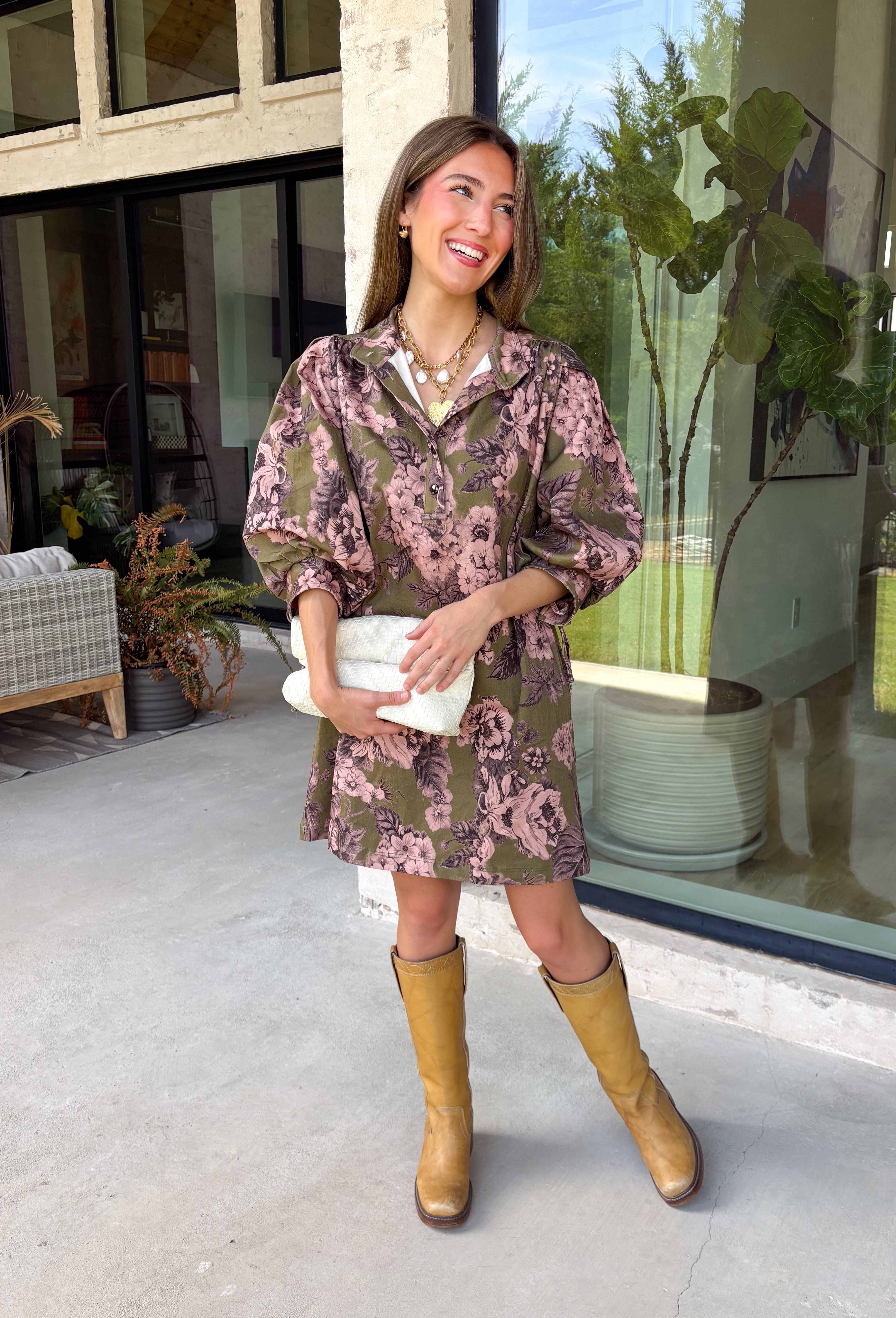 Bring effortless charm to your fall wardrobe with this beautifully detailed dress from Entro. Designed in a rich olive hue with a delicate floral print in shades of light pink and black, this timeless dress is perfect for everything from brunch dates to weekend outings. The stand neckline and partial button-front closure create a polished silhouette, while the ¾ puff sleeves are finished with sweet tie cuffs for an extra feminine touch. 