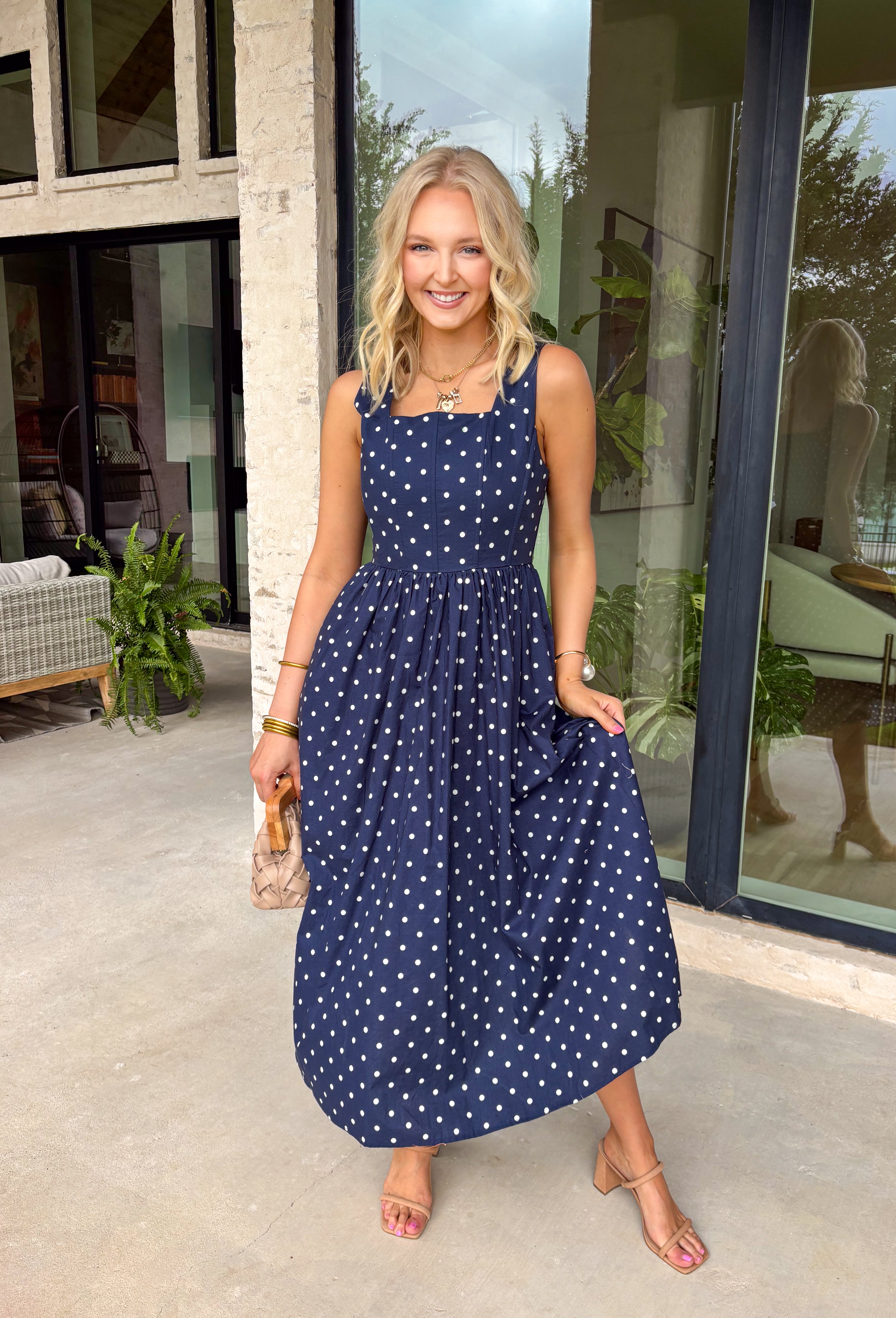 Timeless, feminine, and effortlessly polished! This navy midi dress features a classic white polka dot print that never goes out of style. The square neckline creates a flattering, structured silhouette, while the sleeveless design keeps it light and perfect for warm days. Smocking along the back bodice provides comfortable stretch and a beautiful fit, while the back zipper closure keeps the look clean and tailored. Finished with side pockets and breathable cotton fabric.