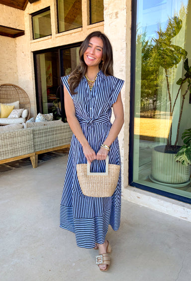 Classic, crisp, and perfect for spring days, this light blue midi dress by Entro is an effortless favorite. Featuring a navy stripe print throughout, it has a timeless look with a flattering, feminine silhouette. The collared neckline and front button details keep it polished, while the matching self-tie belt cinches the waist for an adjustable fit. A flared skirt adds beautiful movement, and side pockets (because yes) make it as practical as it is pretty. With an elastic back waist and lining, this dress i