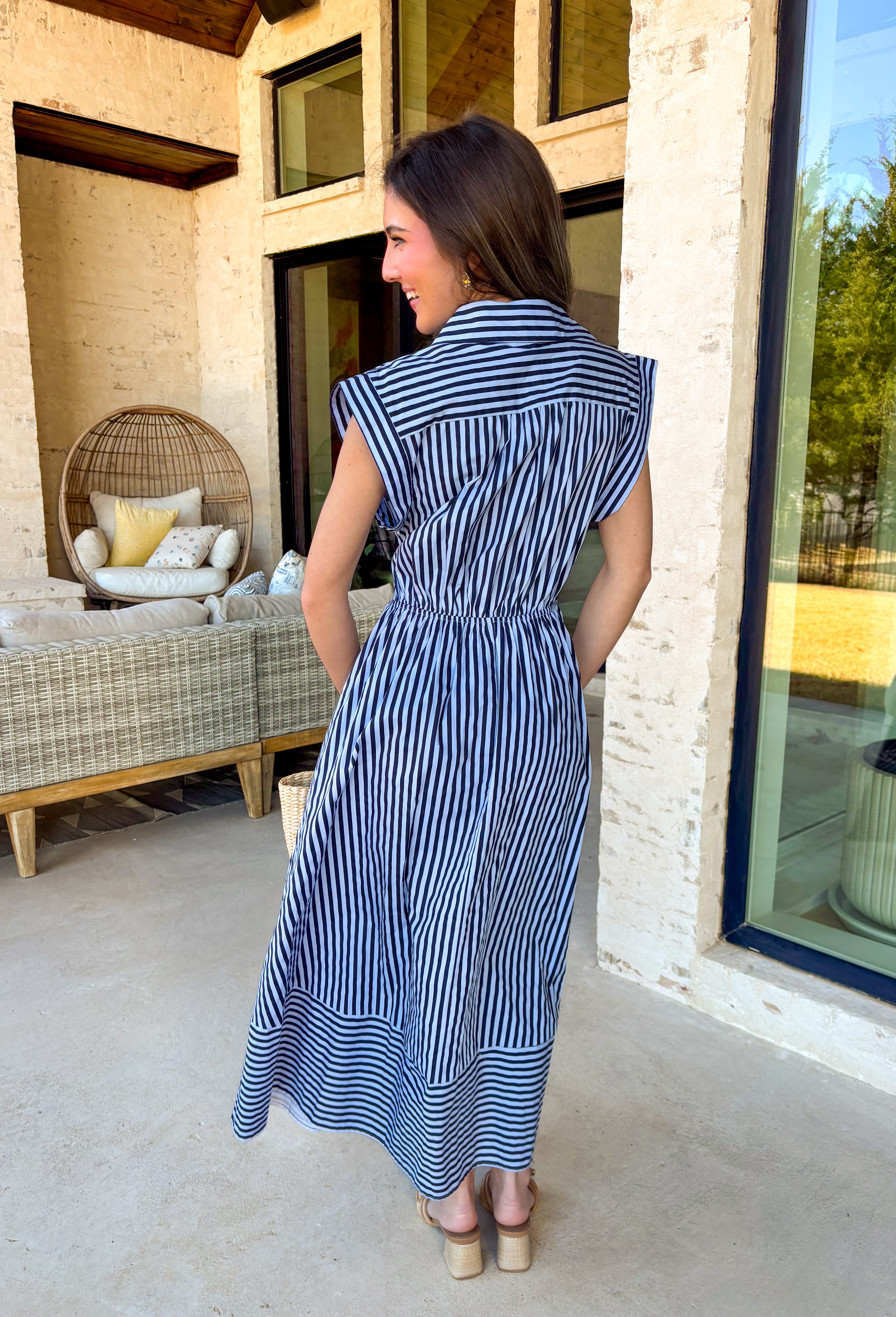 Classic, crisp, and perfect for spring days, this light blue midi dress by Entro is an effortless favorite. Featuring a navy stripe print throughout, it has a timeless look with a flattering, feminine silhouette. The collared neckline and front button details keep it polished, while the matching self-tie belt cinches the waist for an adjustable fit. A flared skirt adds beautiful movement, and side pockets (because yes) make it as practical as it is pretty. With an elastic back waist and lining, this dress i