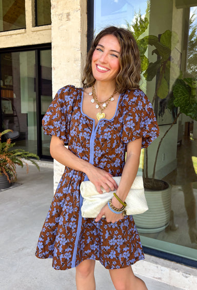 Bring timeless elegance to your fall wardrobe with this beautifully detailed dress from Entro. Designed with a rich brown backdrop and a stunning blue floral print, this feminine dress is full of eye-catching seasonal charm. The flattering square neckline is accented with beautiful blue contrast trim, while the pleated waist creates a flattering, defined silhouette. 