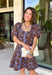 Bring timeless elegance to your fall wardrobe with this beautifully detailed dress from Entro. Designed with a rich brown backdrop and a stunning blue floral print, this feminine dress is full of eye-catching seasonal charm. The flattering square neckline is accented with beautiful blue contrast trim, while the pleated waist creates a flattering, defined silhouette. 