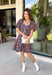 Bring timeless elegance to your fall wardrobe with this beautifully detailed dress from Entro. Designed with a rich brown backdrop and a stunning blue floral print, this feminine dress is full of eye-catching seasonal charm. The flattering square neckline is accented with beautiful blue contrast trim, while the pleated waist creates a flattering, defined silhouette. 