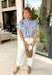 Bright, cheerful, and full of spring personality, this light blue button-down top by Entro is an instant outfit-lifter. Featuring a colorful floral print with pops of pink, green, red, and yellow, it brings a playful feel to a classic silhouette. The blue and white striped sleeves and neckline add a fun contrast, while the subtle ruffle neckline gives it a soft, feminine finish. Lightweight cotton makes it perfect for warm days and easy layering.