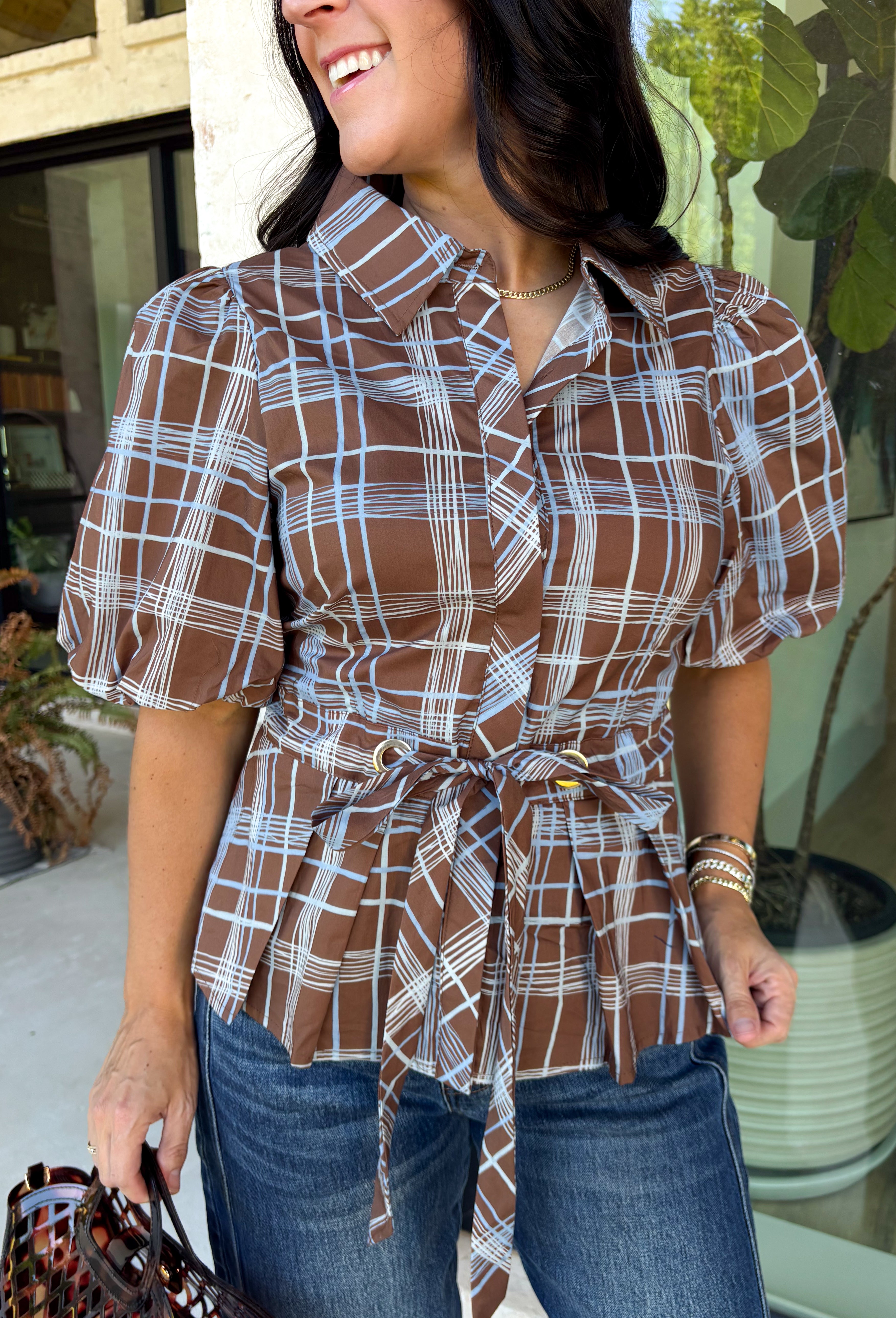 Classic plaid gets a fresh fall update with this brown and blue blouse from Entro. The mix of warm brown and cool blue creates an eye-catching color combination that fits right into your autumn wardrobe. A shirt collar and button-front closure give it a classic feel, while pleated detailing at the front and back adds shape and texture. The self-tie belt lets you define the waist, and the peplum hem creates a flattering finish that's perfect with denim or trousers. 
