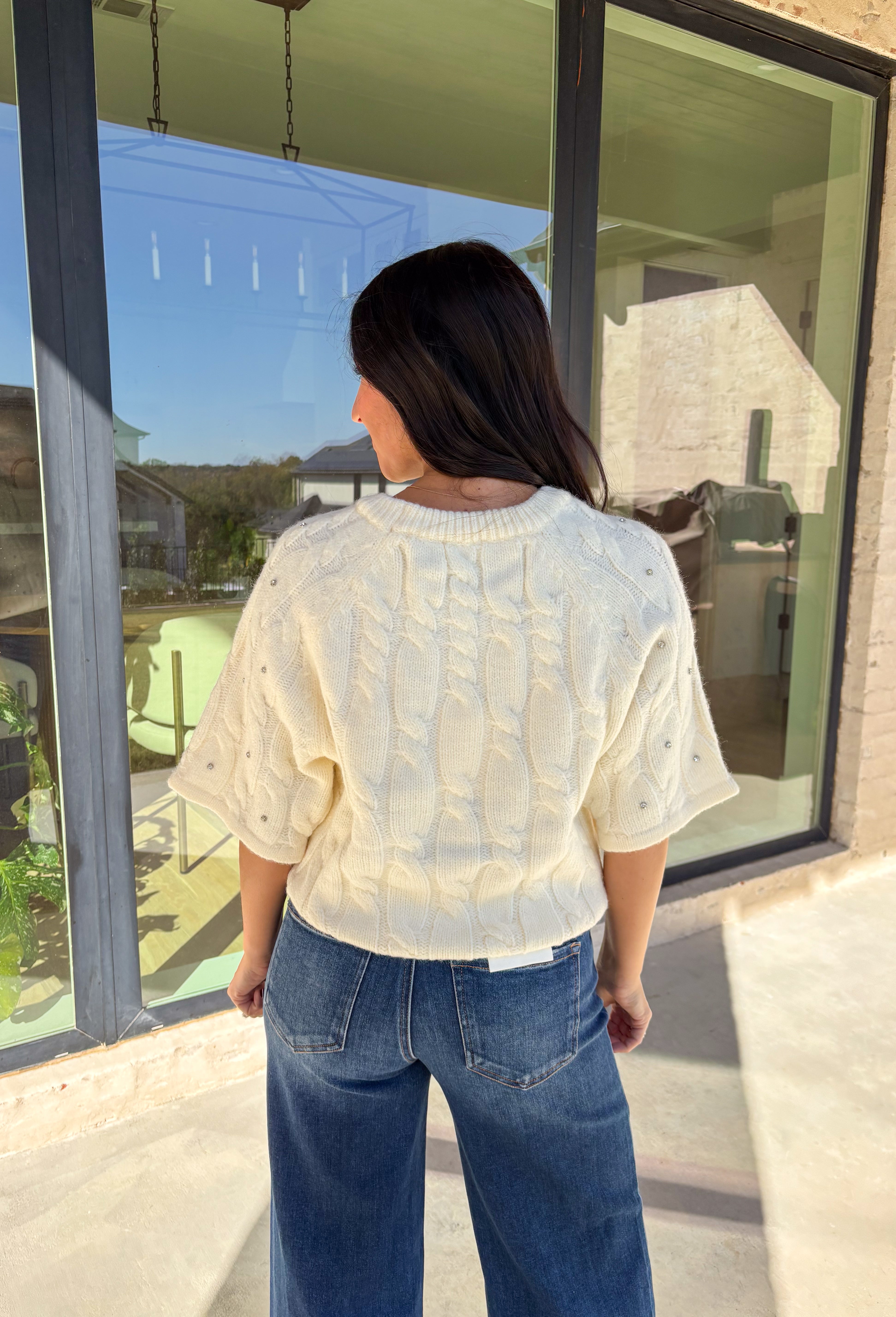 Add a little sparkle to your holiday style with this cream cable knit sweater by Entro. Featuring short sleeves and delicate crystal embellishments on the front, this cozy knit is the perfect mix of classic and festive. The soft texture and timeless cable design make it an easy choice for everything from office parties to family gatherings.