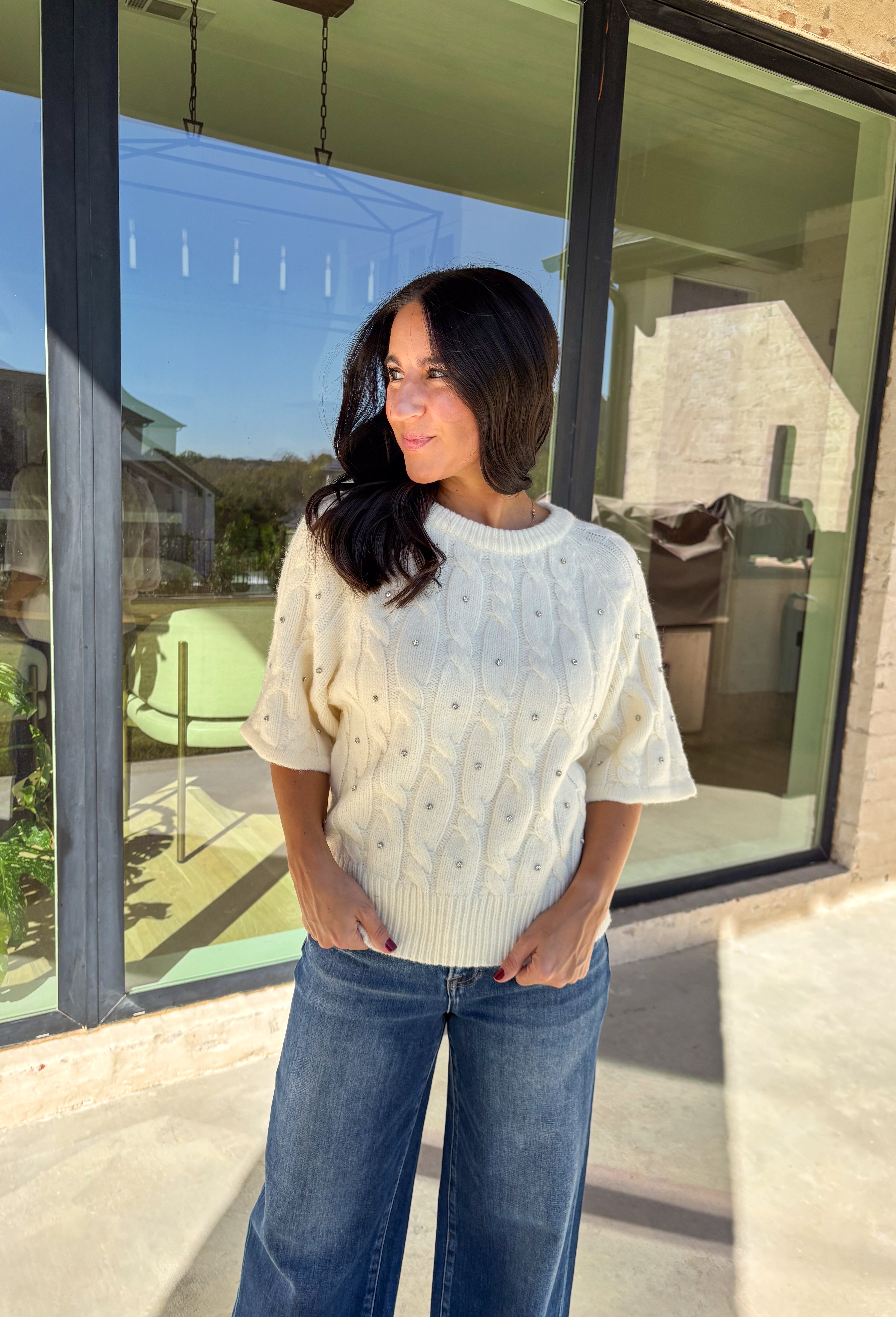 Add a little sparkle to your holiday style with this cream cable knit sweater by Entro. Featuring short sleeves and delicate crystal embellishments on the front, this cozy knit is the perfect mix of classic and festive. The soft texture and timeless cable design make it an easy choice for everything from office parties to family gatherings.