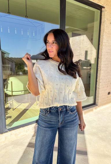 Add a little sparkle to your holiday style with this cream cable knit sweater by Entro. Featuring short sleeves and delicate crystal embellishments on the front, this cozy knit is the perfect mix of classic and festive. The soft texture and timeless cable design make it an easy choice for everything from office parties to family gatherings.