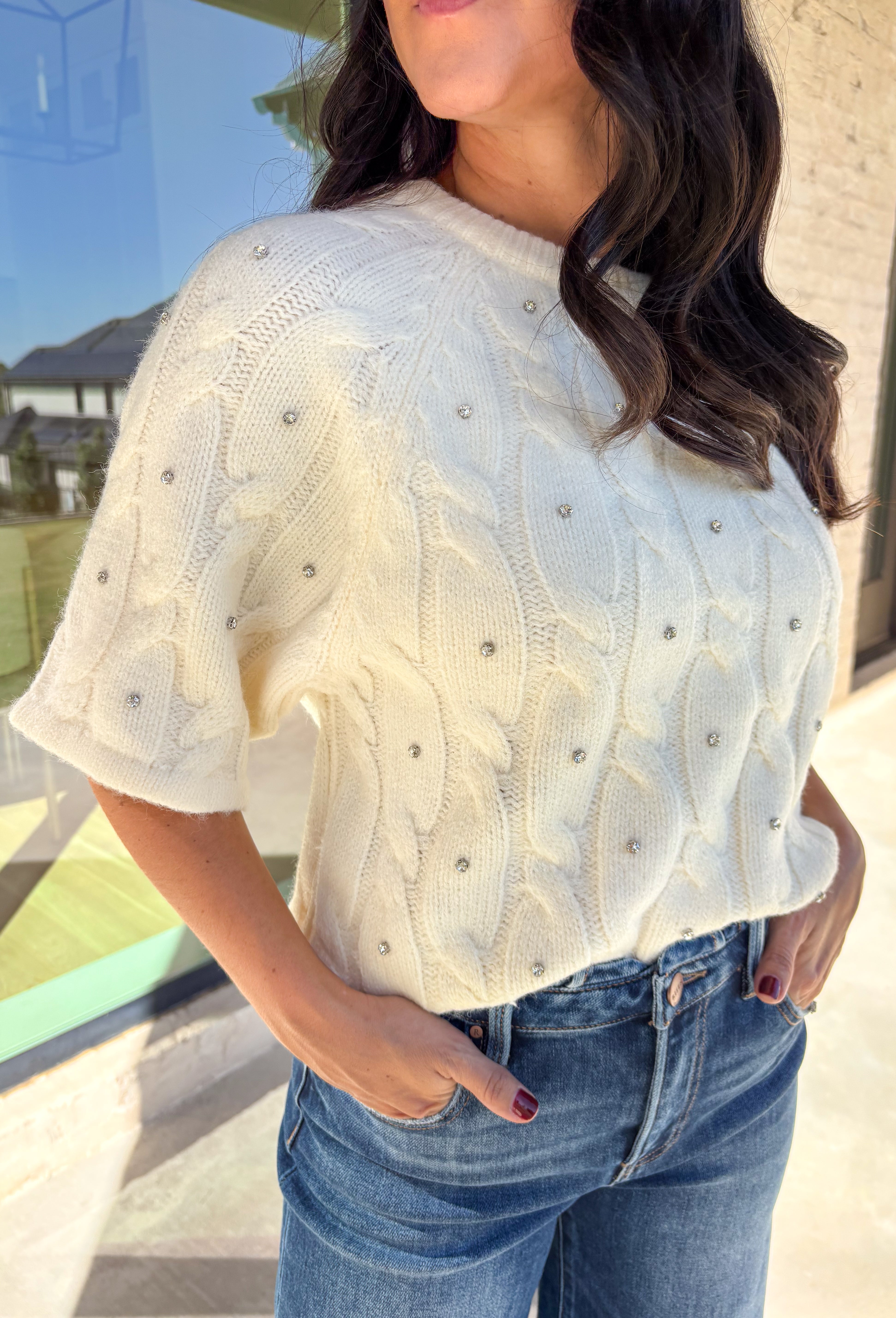 Add a little sparkle to your holiday style with this cream cable knit sweater by Entro. Featuring short sleeves and delicate crystal embellishments on the front, this cozy knit is the perfect mix of classic and festive. The soft texture and timeless cable design make it an easy choice for everything from office parties to family gatherings.