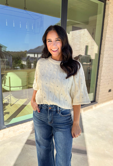 Add a little sparkle to your holiday style with this cream cable knit sweater by Entro. Featuring short sleeves and delicate crystal embellishments on the front, this cozy knit is the perfect mix of classic and festive. The soft texture and timeless cable design make it an easy choice for everything from office parties to family gatherings.