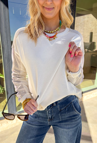 Lightweight and cozy, this off-white pullover by Mystree is an easy go-to for everyday wear. The washed gray and lavender details on the sleeves add a subtle pop of color and personality, while the breathable cotton fabric keeps it comfortable all day long. Perfect for layering or wearing solo, it’s a versatile piece that fits right into your fall wardrobe.